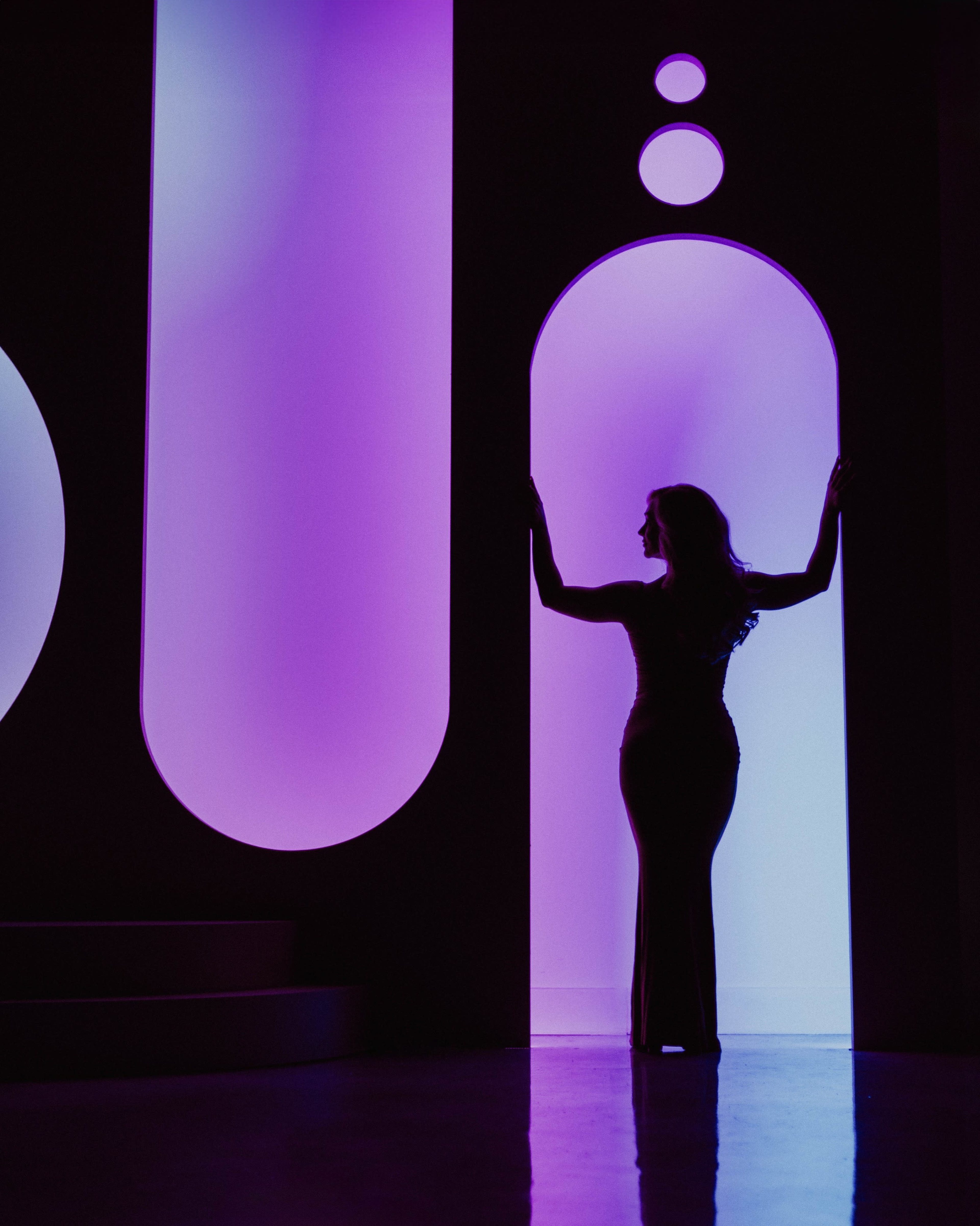 A silhouetted figure stands in an archway illuminated by vibrant purple and blue lights.