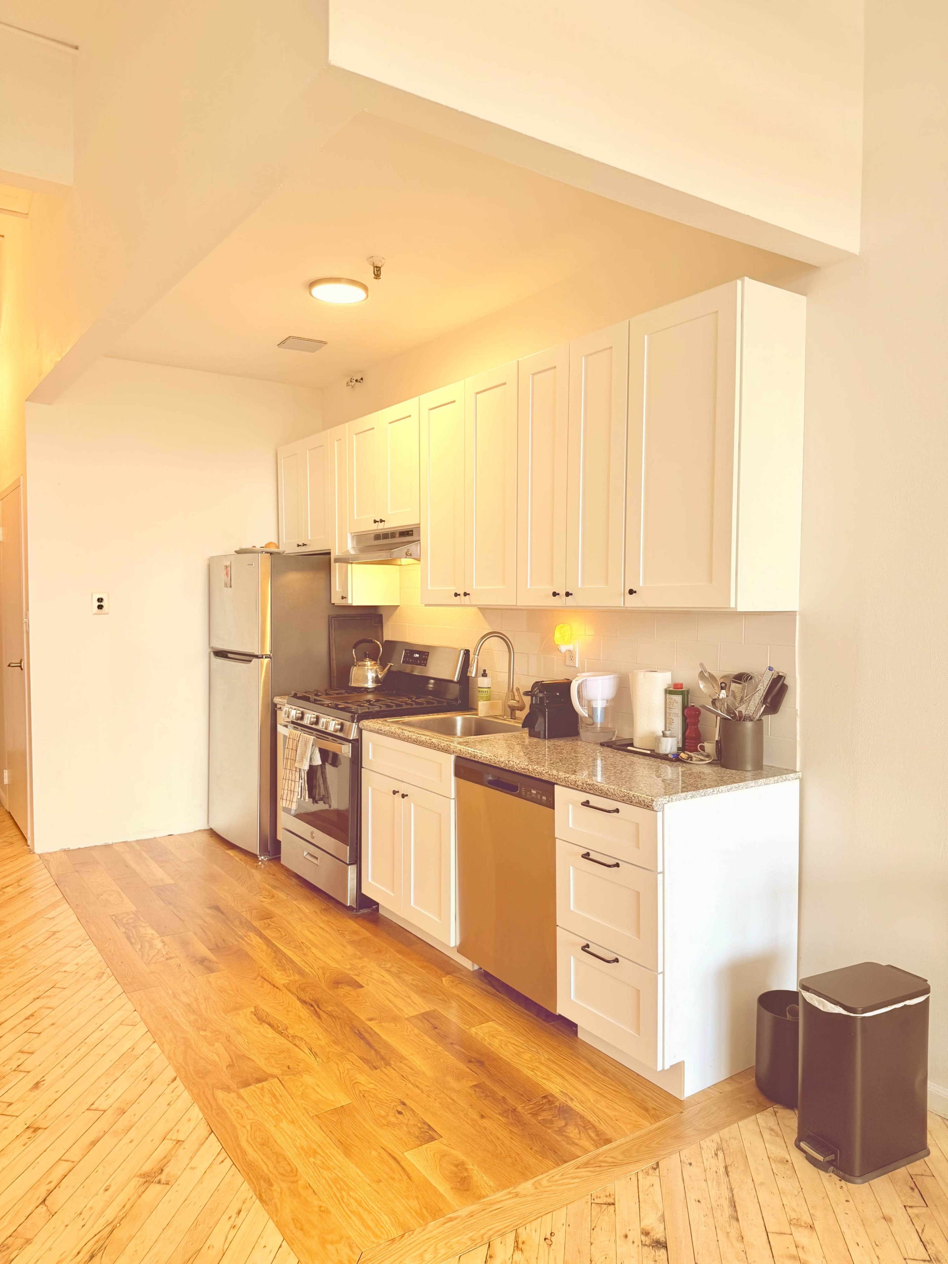 A modern kitchen with white cabinets, stainless steel appliances, and a wooden floor.