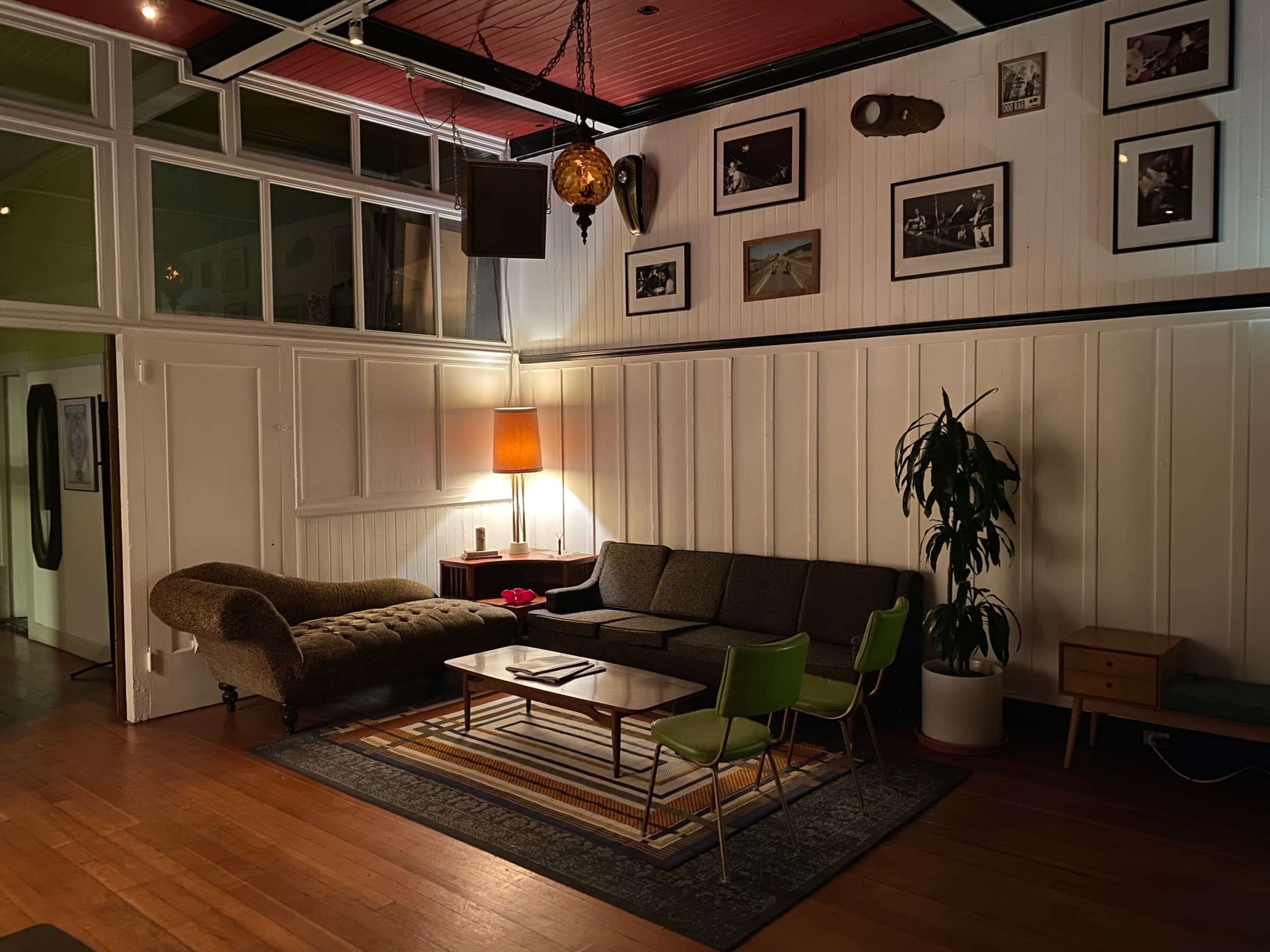 A cozy living room features a dark sofa, green chairs, a coffee table, and various framed photographs on the walls.