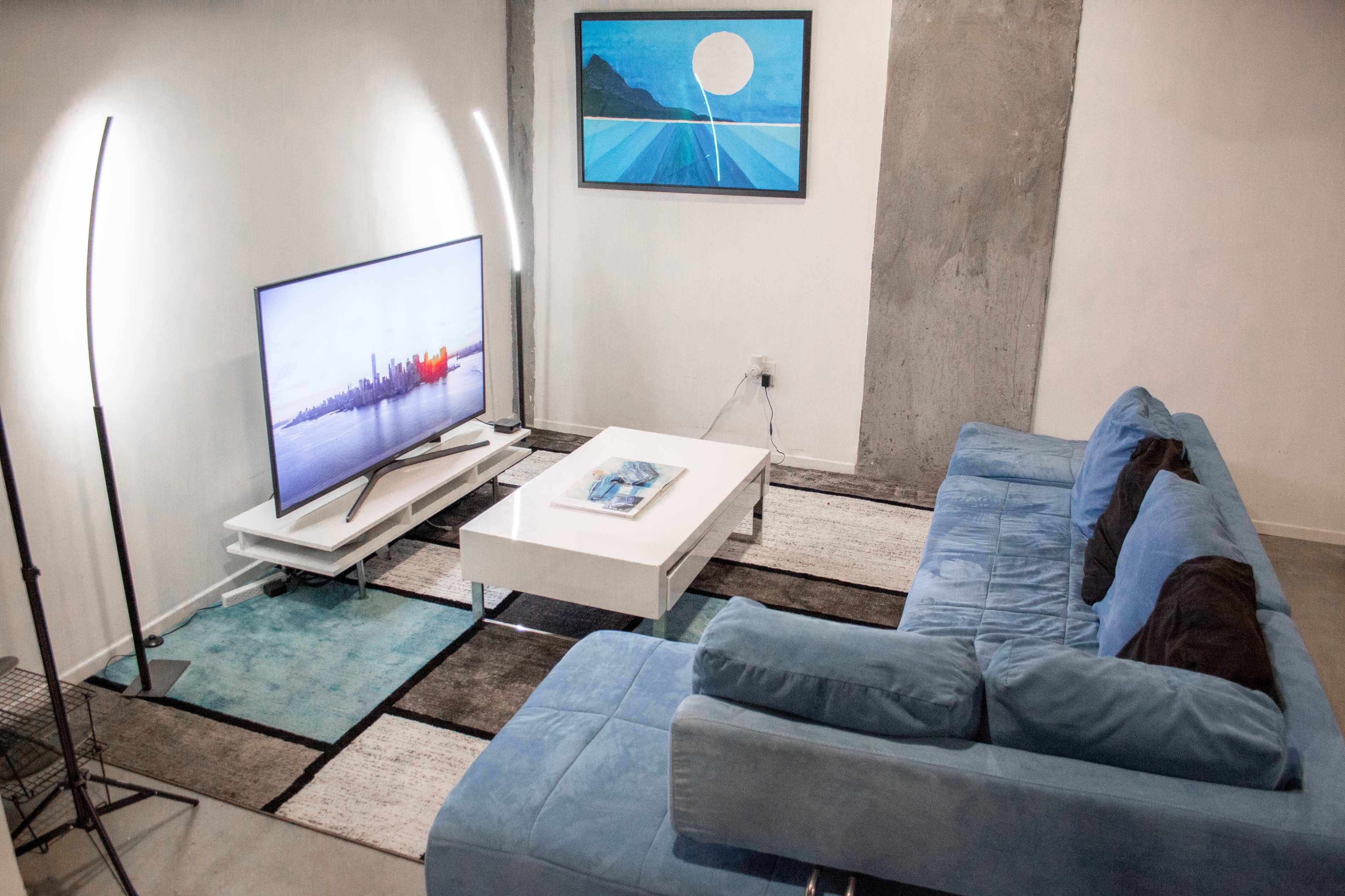 A modern living room with a blue sectional sofa, a white coffee table, and a television displaying a cityscape.