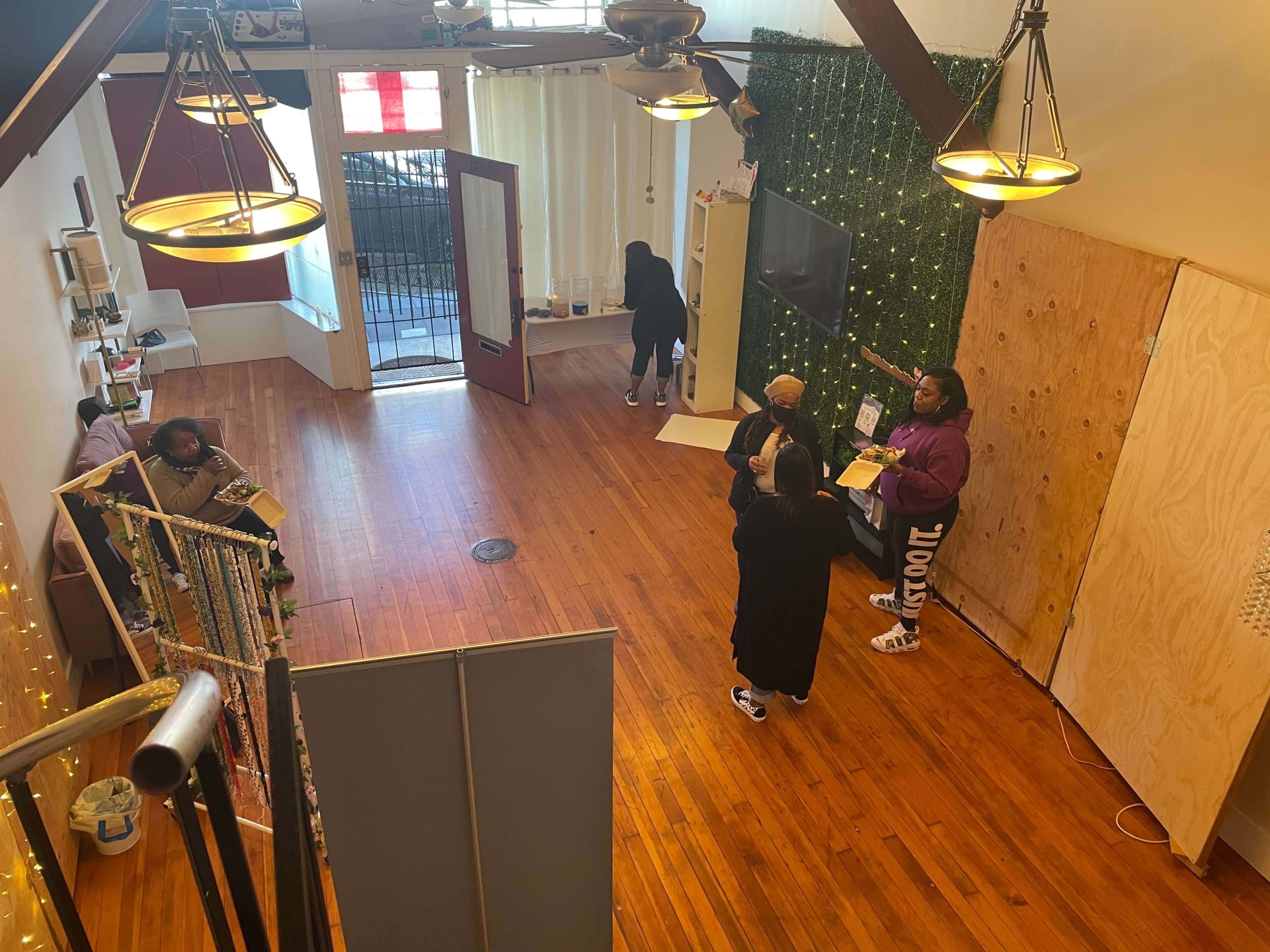 A spacious room with wooden flooring and several people engaged in conversation, while a staircase leads to a lower level.