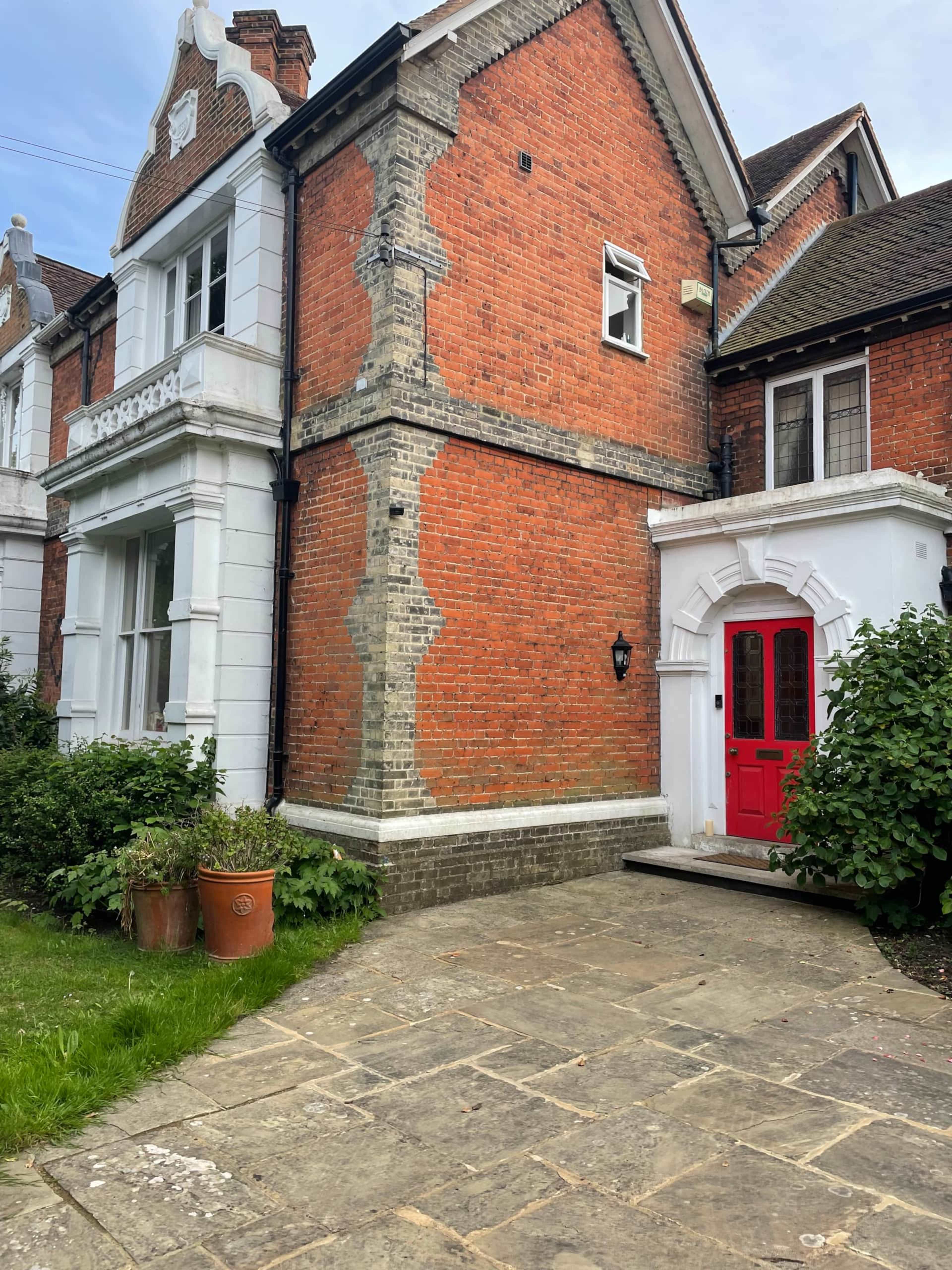 A red door is framed by a brick and white-stucco house with a stone pathway and greenery in the foreground.