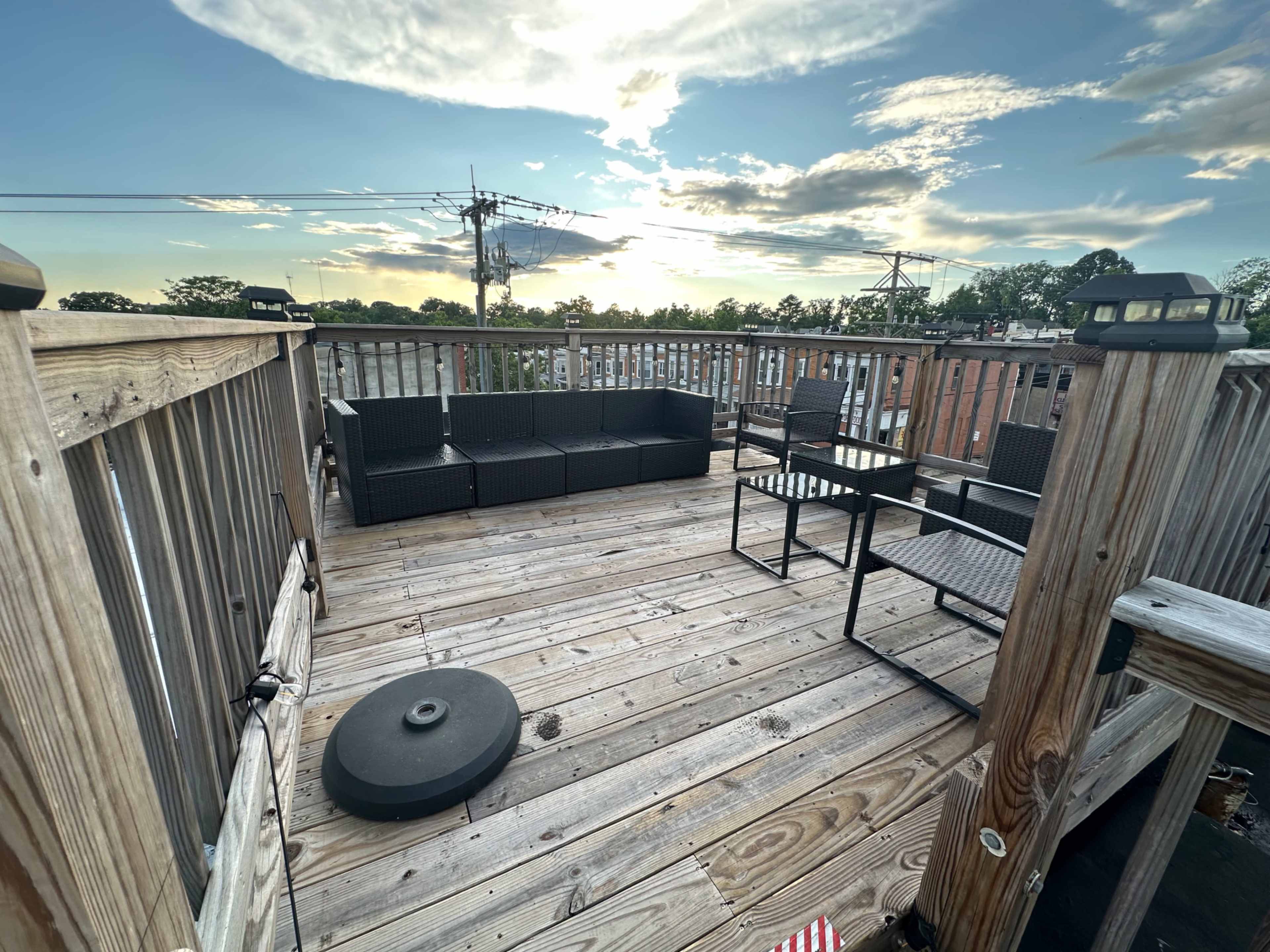 The image shows a wooden rooftop deck with black outdoor furniture and a cloudy sky in the background.