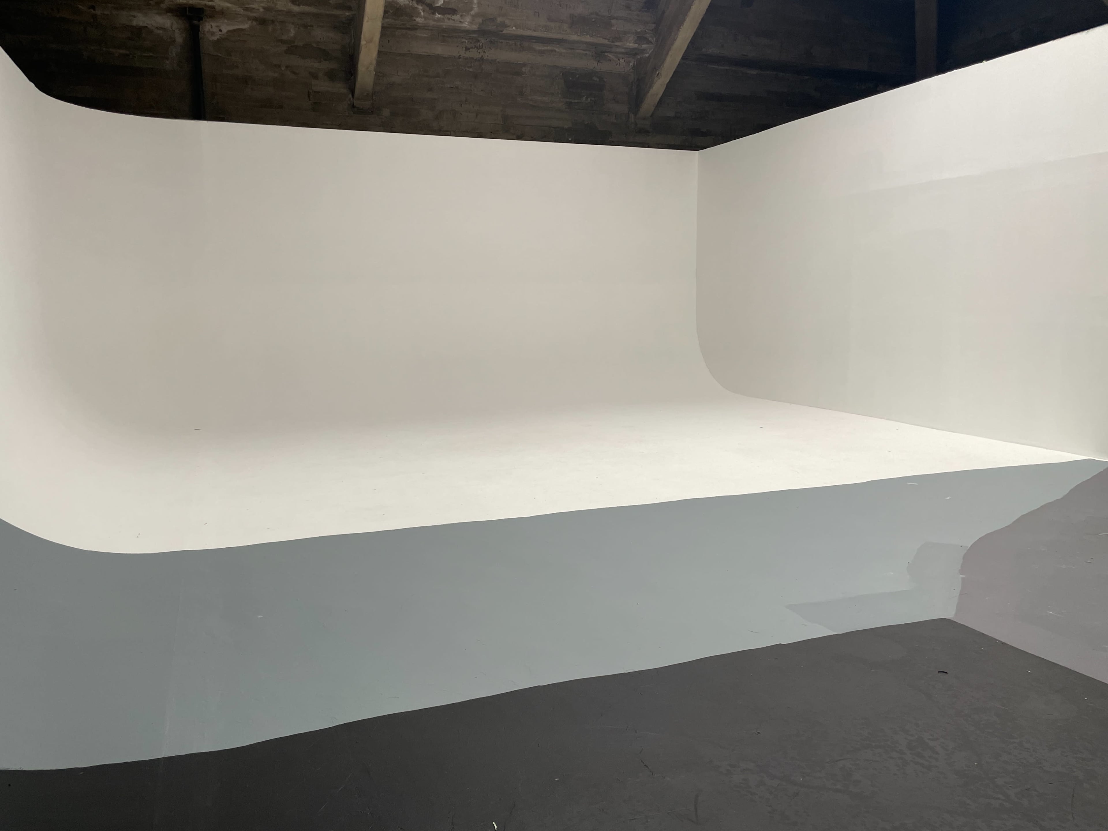 A minimalist indoor space featuring a large, curved white backdrop with a section of gray and black flooring.
