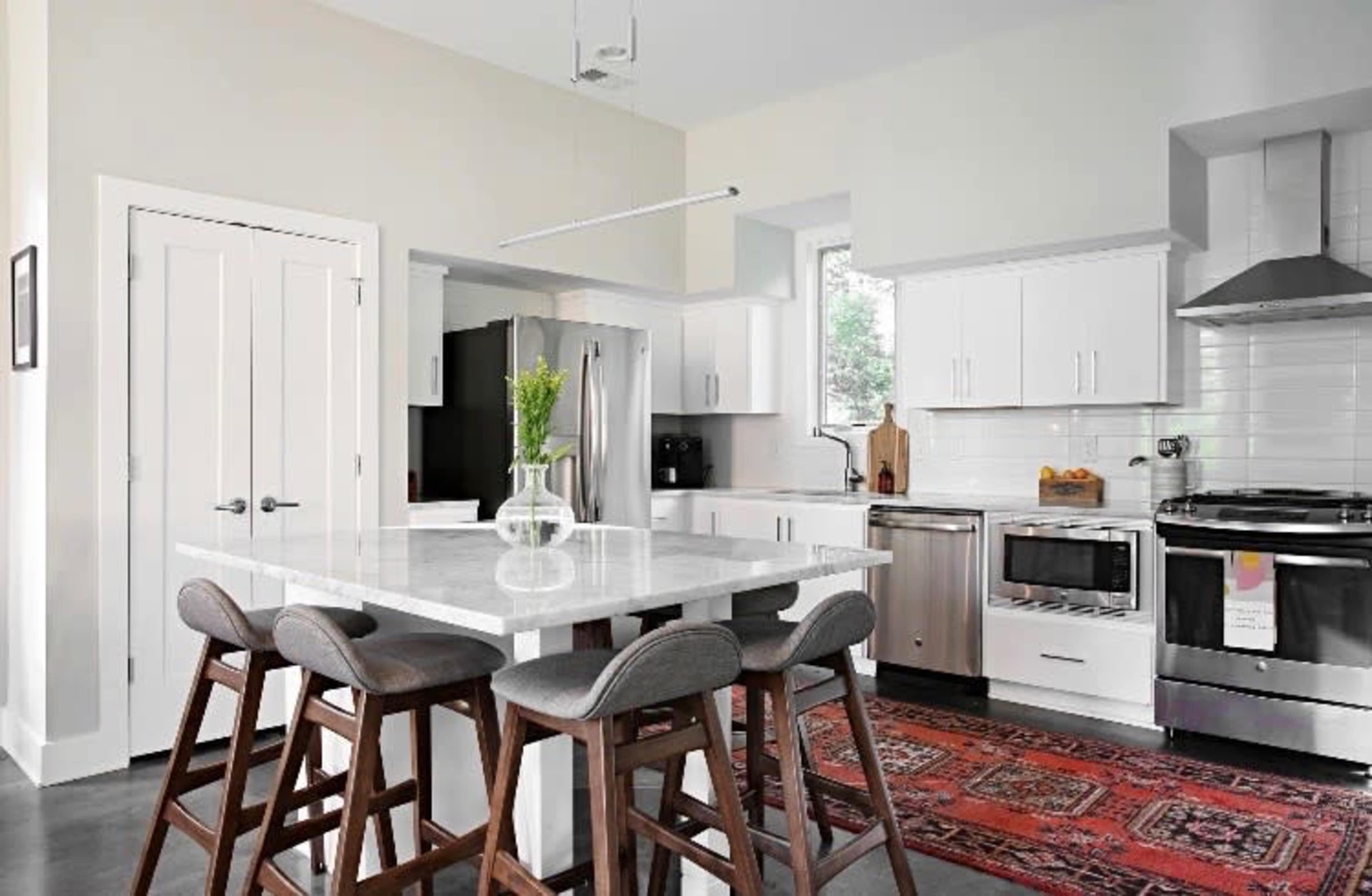A modern kitchen with white cabinetry, stainless steel appliances, and a central island with four wooden stools.