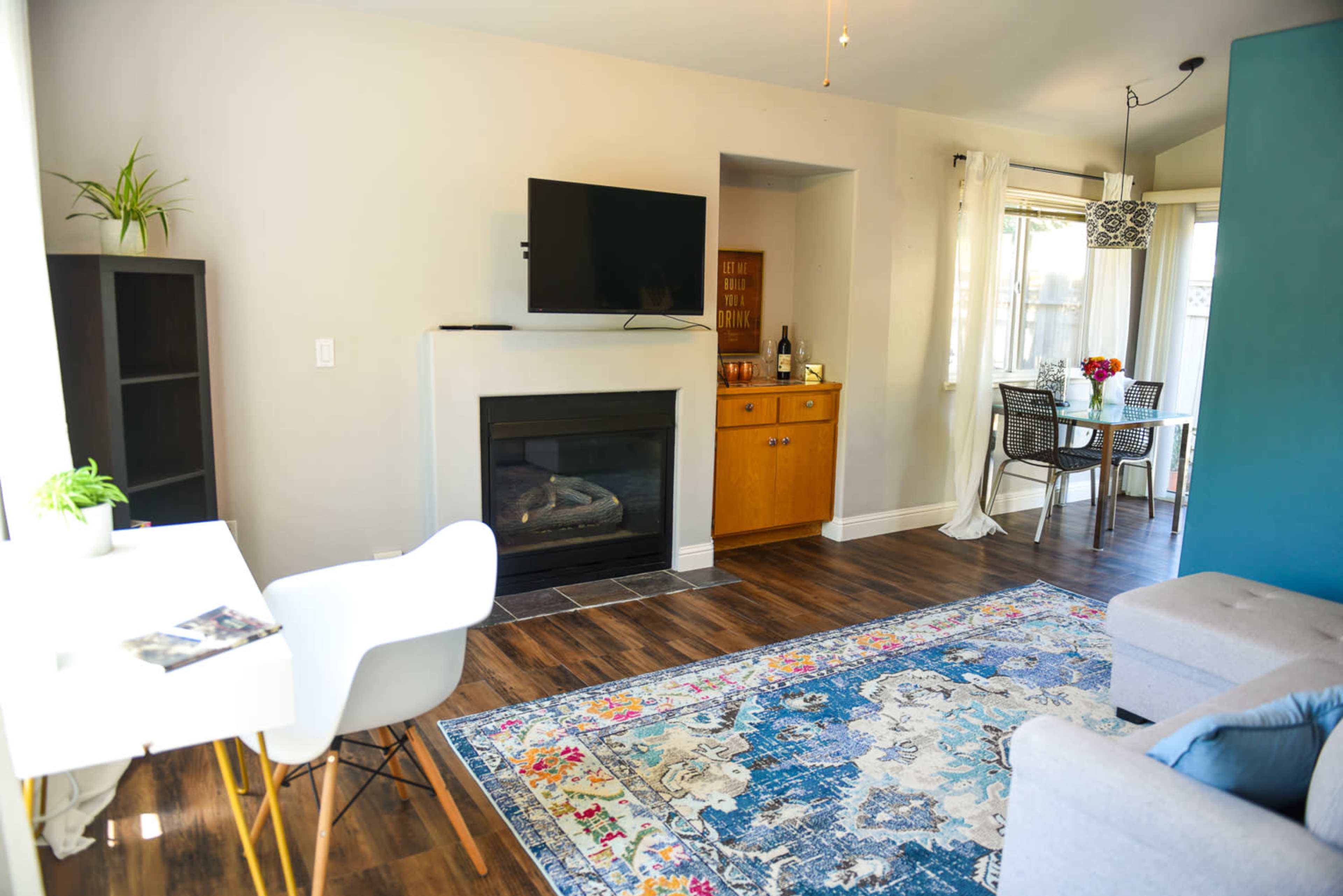 A cozy living room featuring a fireplace, a television mounted on the wall, a dining area with a table and chairs, and a decorative area rug.