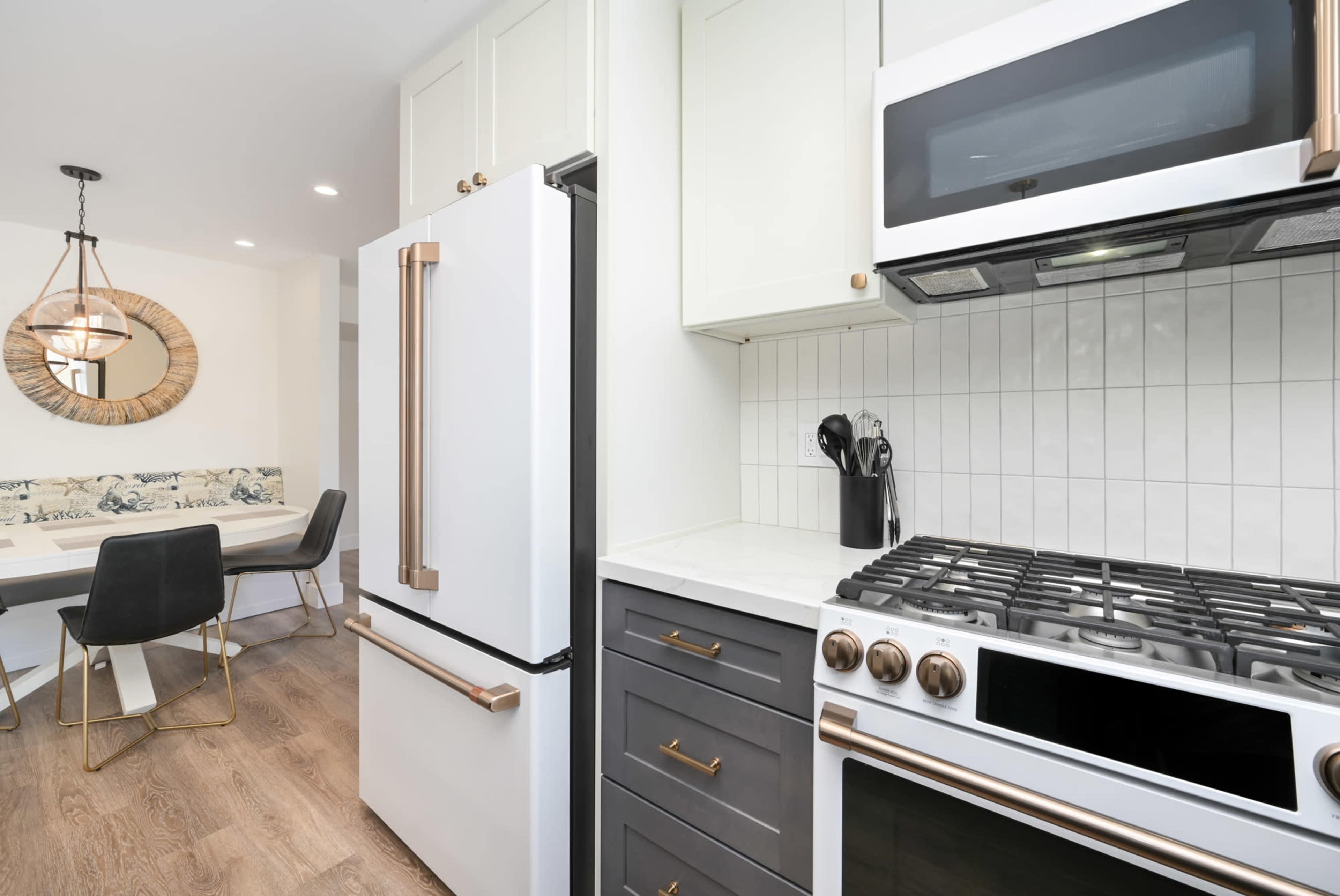 A modern kitchen with stainless steel appliances, including a gas stove and refrigerator, adjacent to a dining area with a round mirror and a white table.
