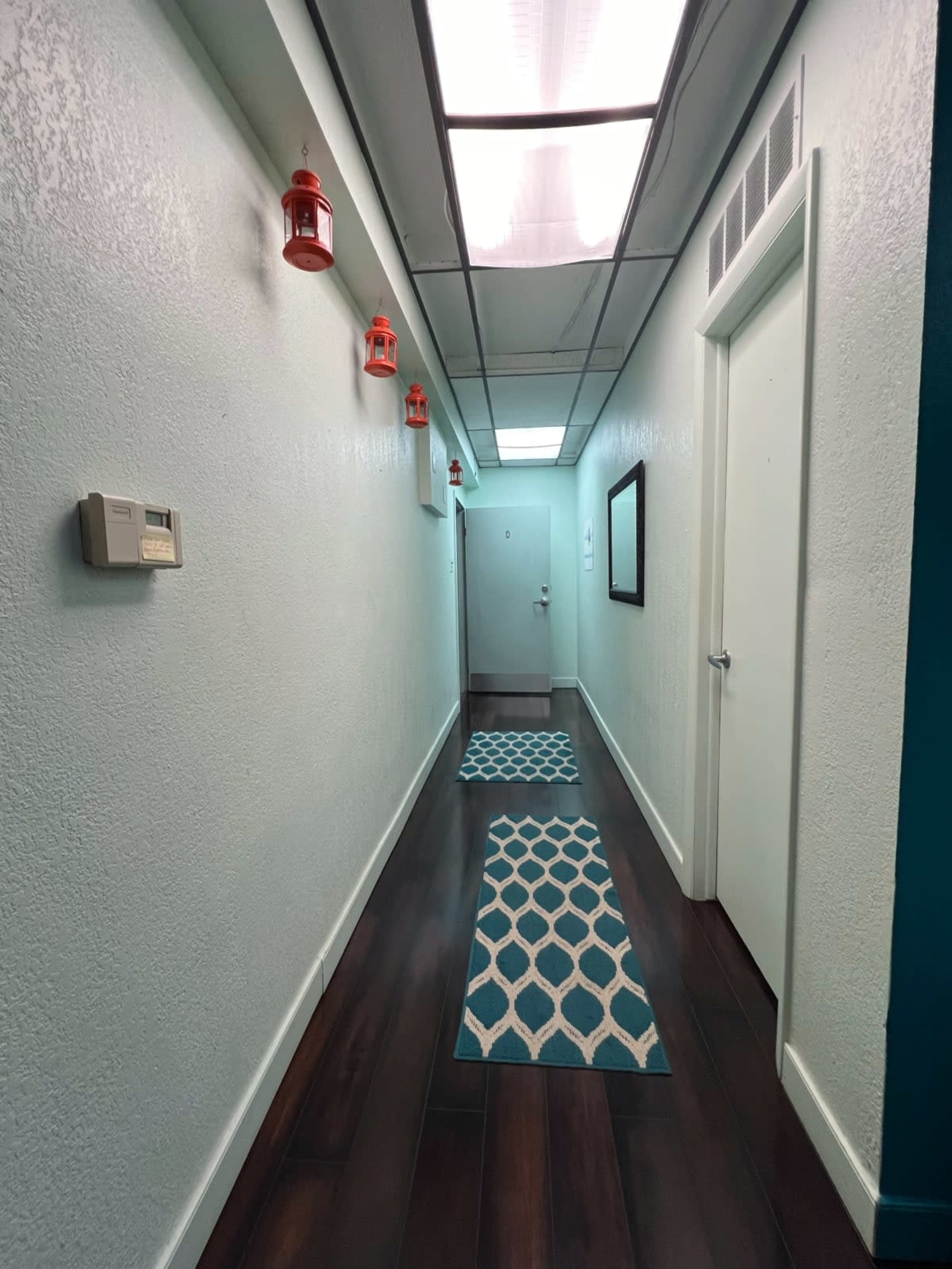 The image shows a narrow hallway with teal-colored walls, wooden flooring, and two patterned rugs along the center.