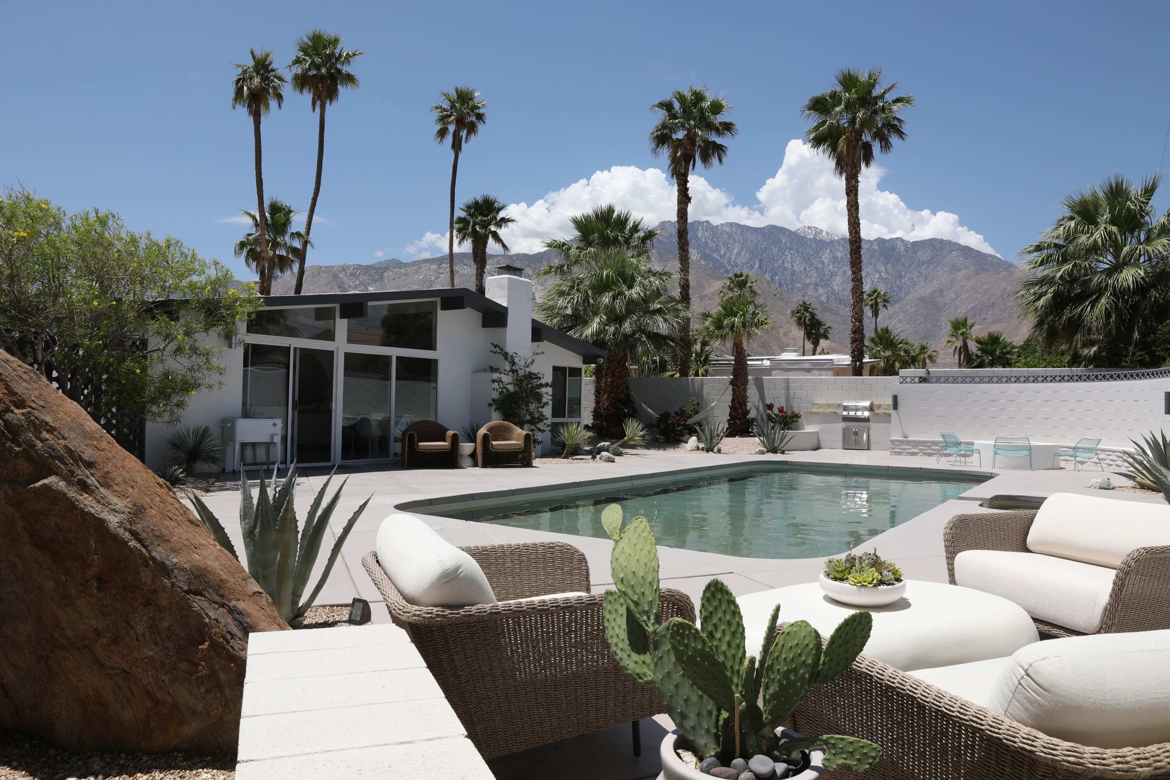 A modern house with a swimming pool, surrounded by palm trees and mountains in the background.