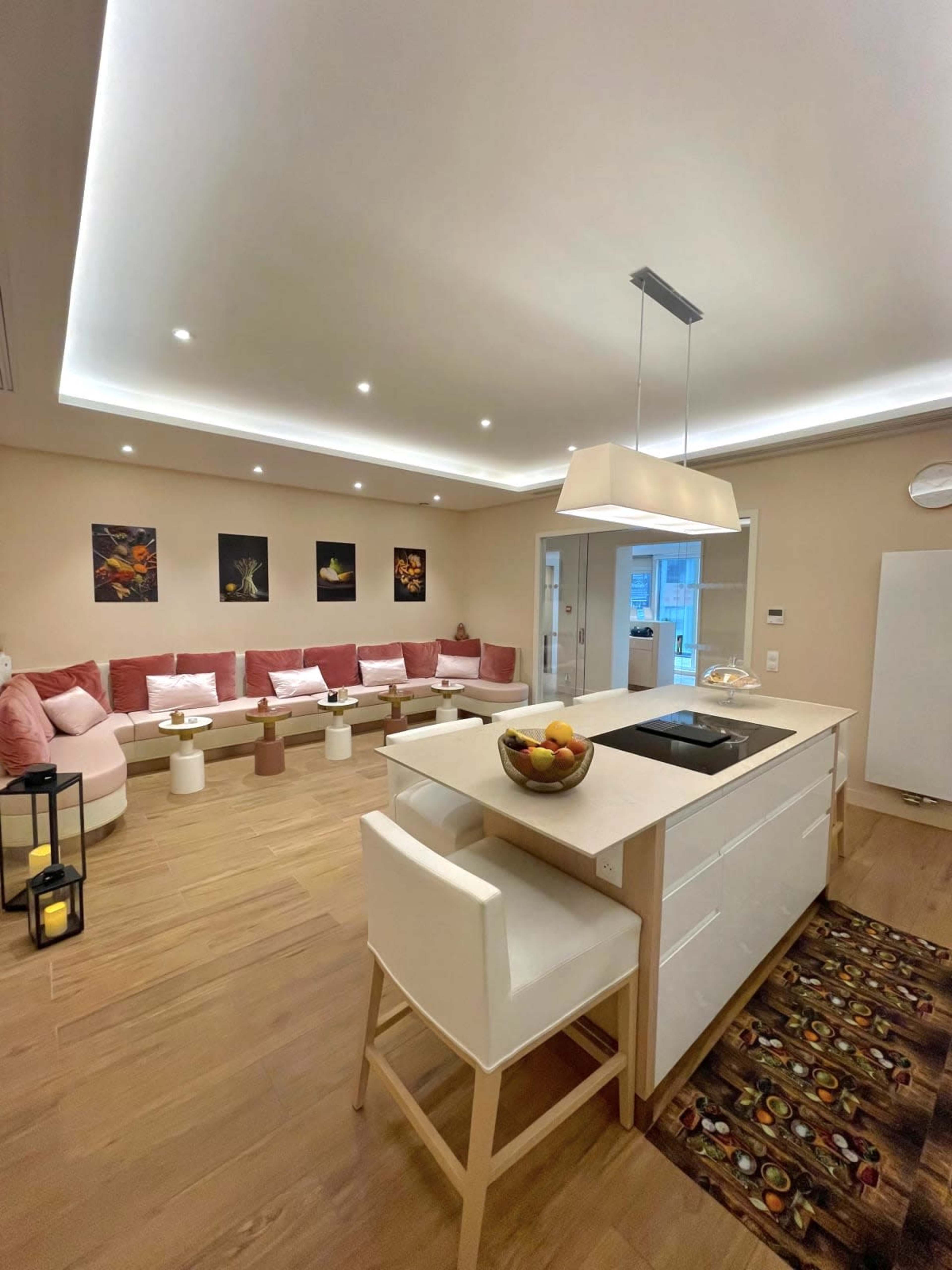 A modern, open-concept living space featuring a kitchen island with seating, a seating area with pink cushions, and decorative wall art.