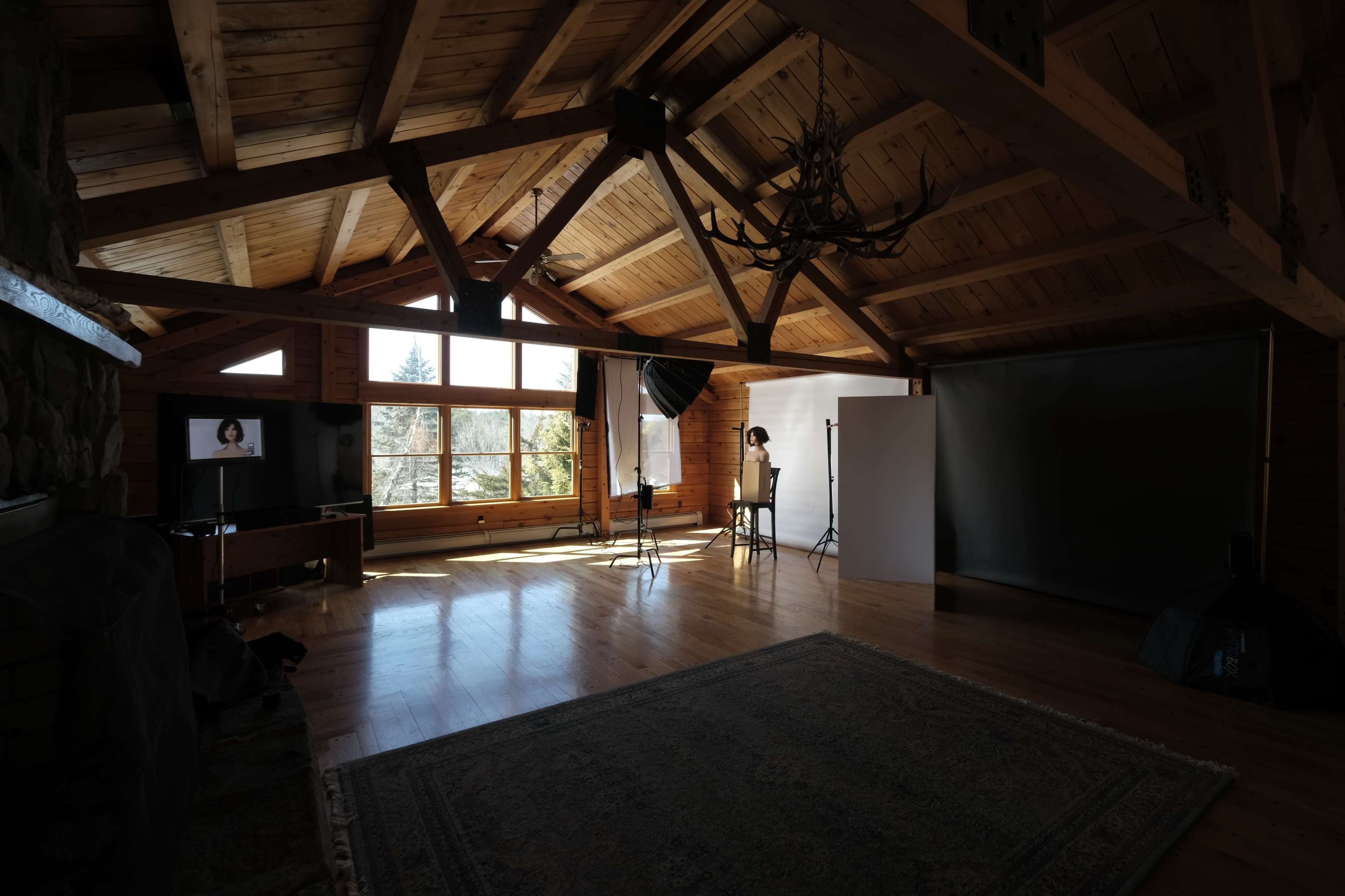 A spacious, rustic studio with wooden beams, large windows, and photography equipment set up in an illuminated area.
