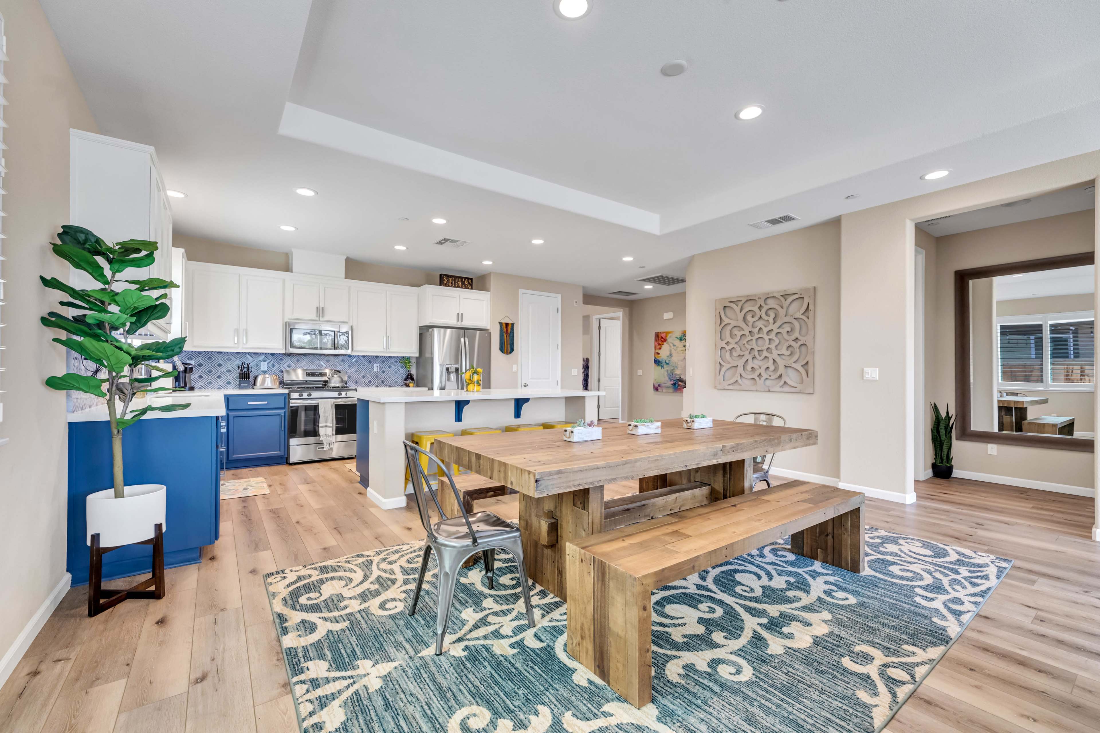 A modern kitchen and dining area with a wooden dining table, patterned rug, and sleek appliances.
