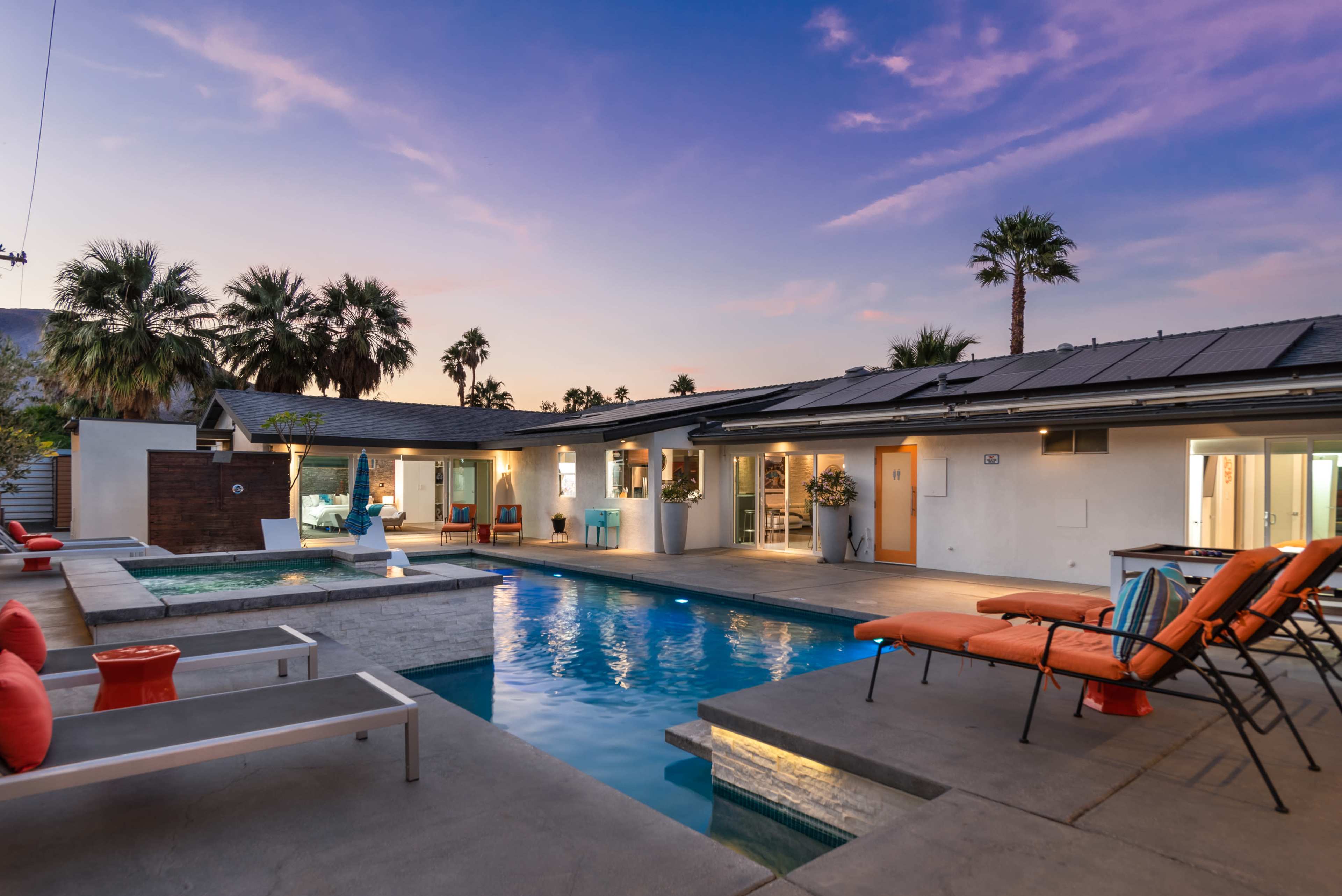 A modern backyard with a swimming pool, lounge chairs, and palm trees under a twilight sky.