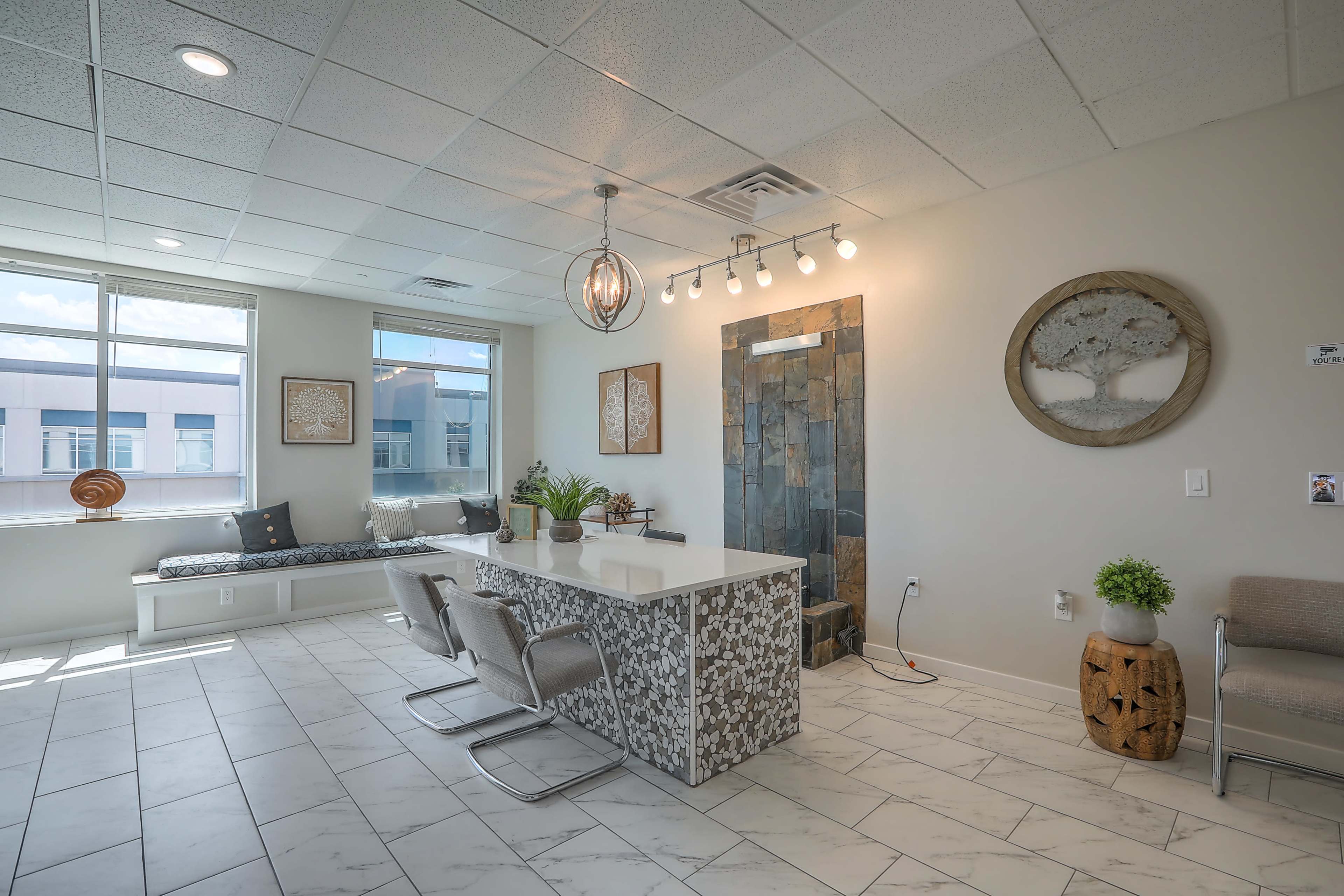 A modern office waiting area featuring a stone accent wall, a white reception desk, seating along the windows, and decorative artwork.