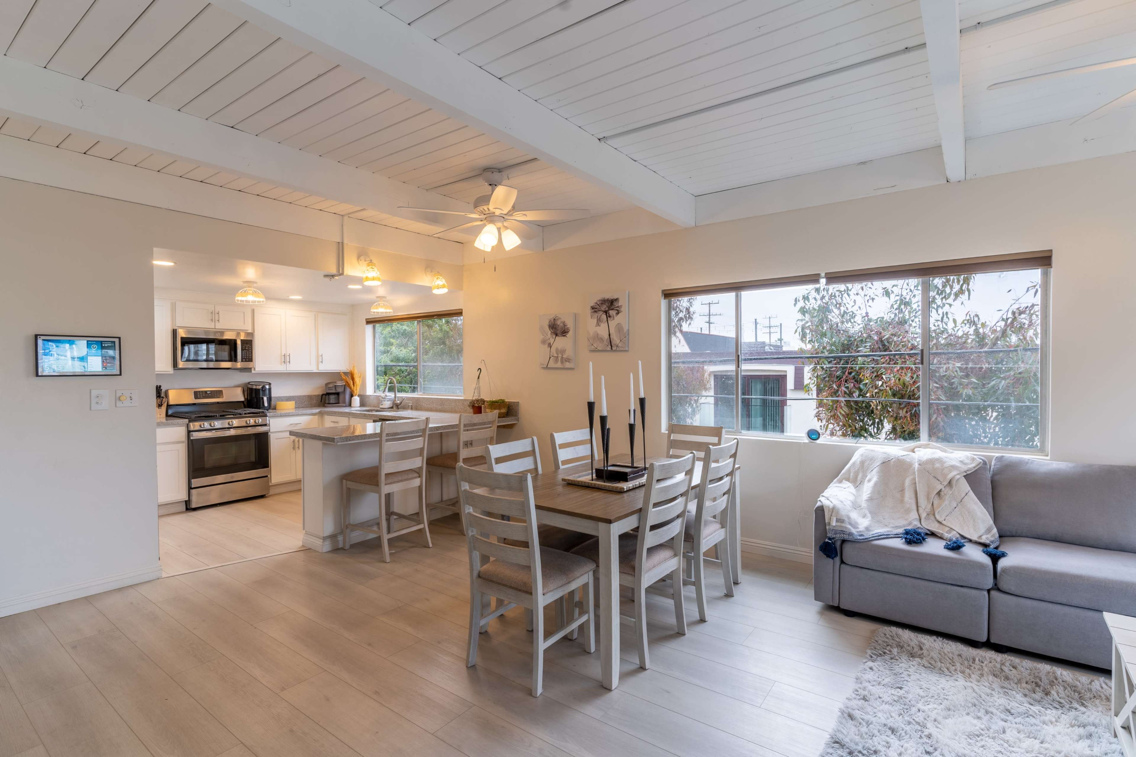 A bright, open living space features a dining area with a table and chairs adjacent to a modern kitchen, all illuminated by overhead lighting.