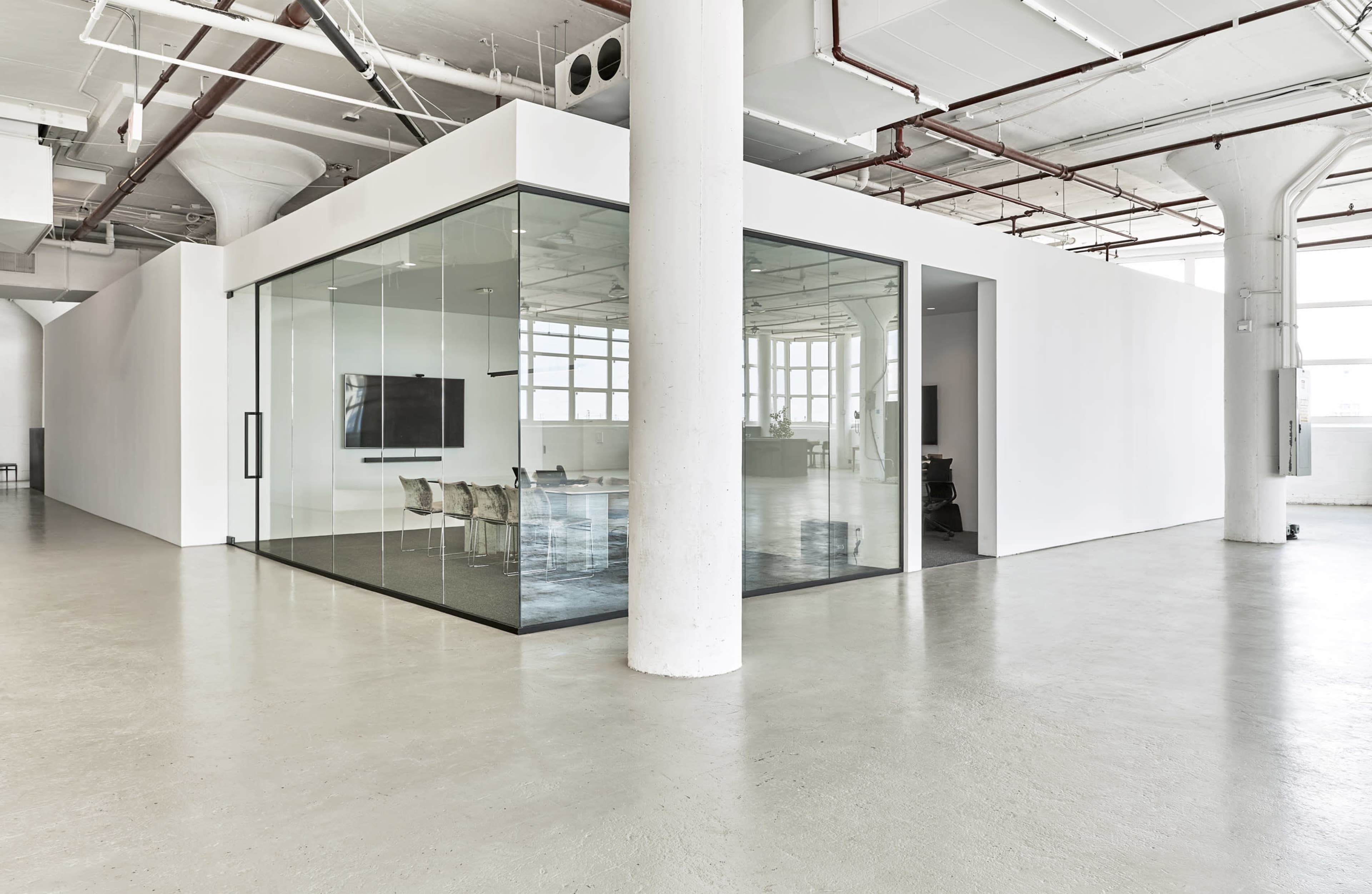 The image shows a spacious, modern office interior featuring a glass meeting room and white walls.