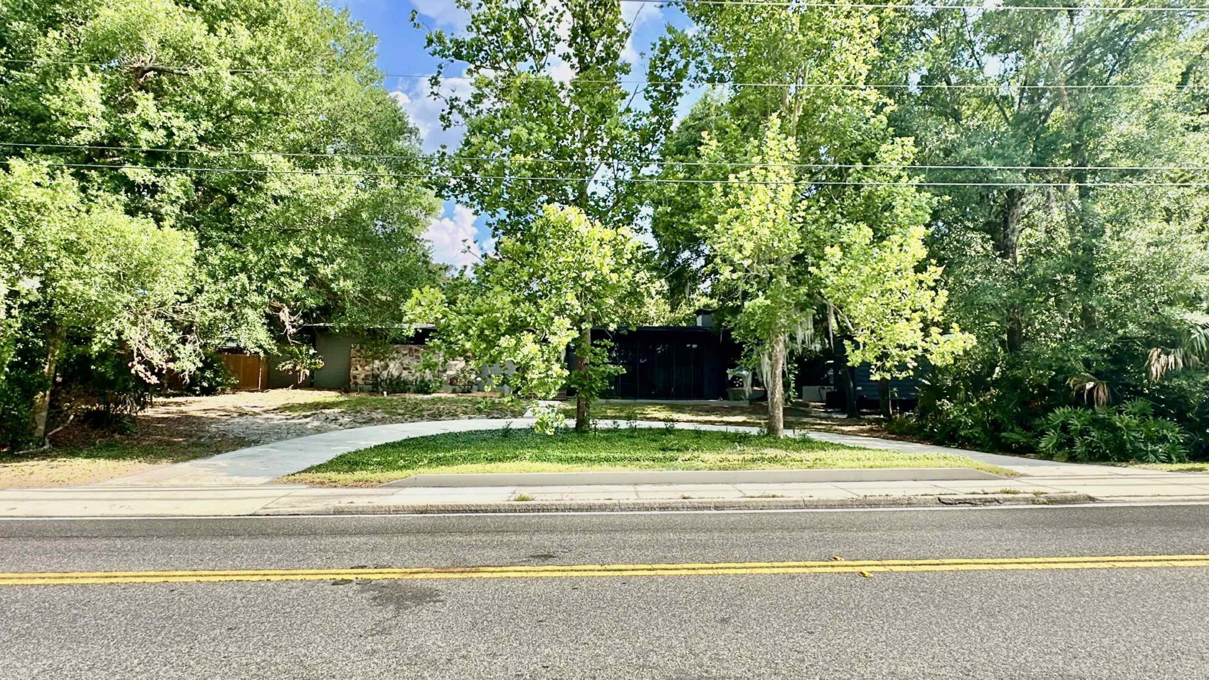 A modern house with a black facade is surrounded by lush green trees and a well-maintained lawn, viewed from across the street.