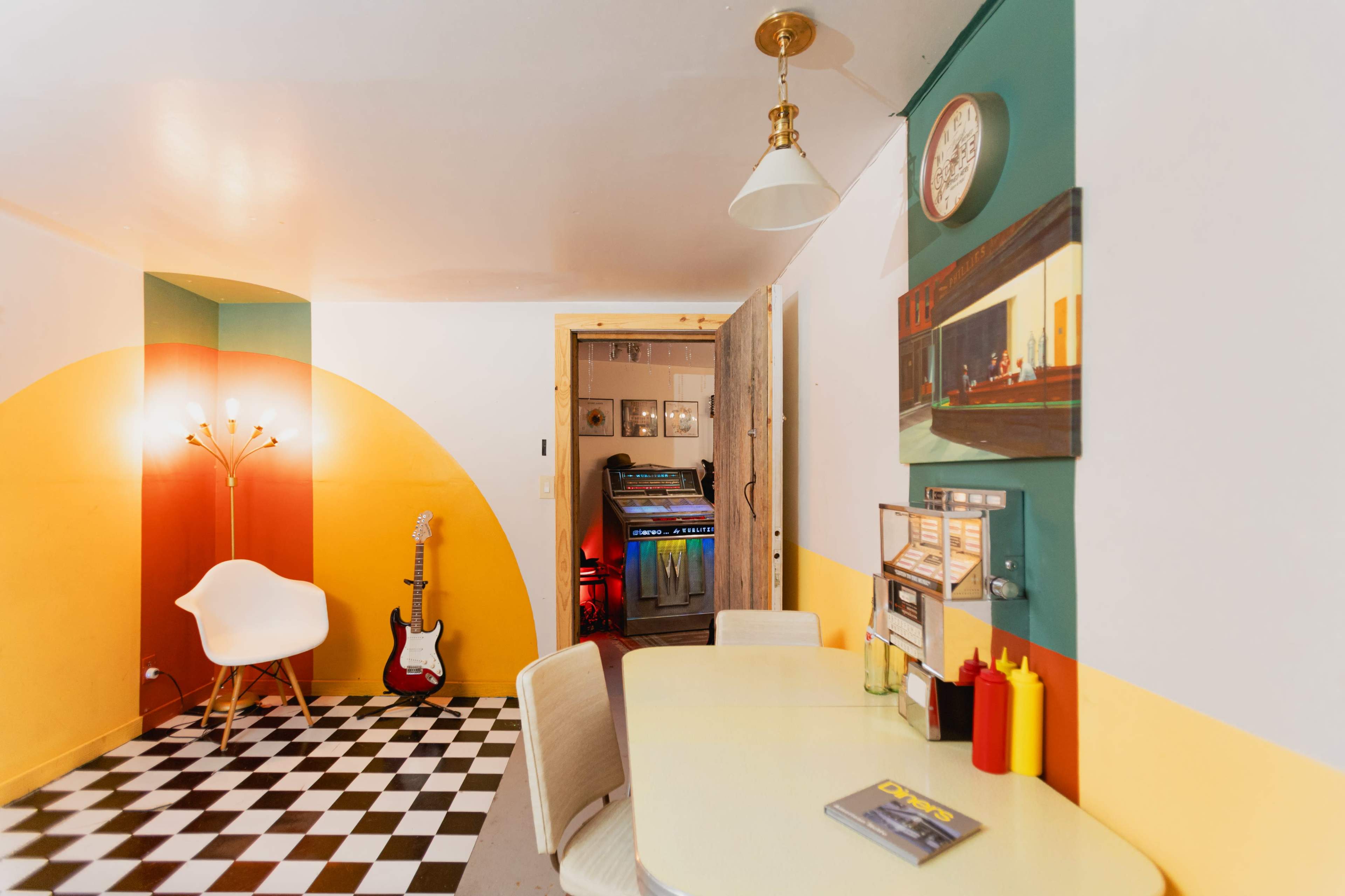 The image shows a vibrant room featuring a yellow and green color scheme, a checkered black and white floor, a modern white chair, and a table with condiments.