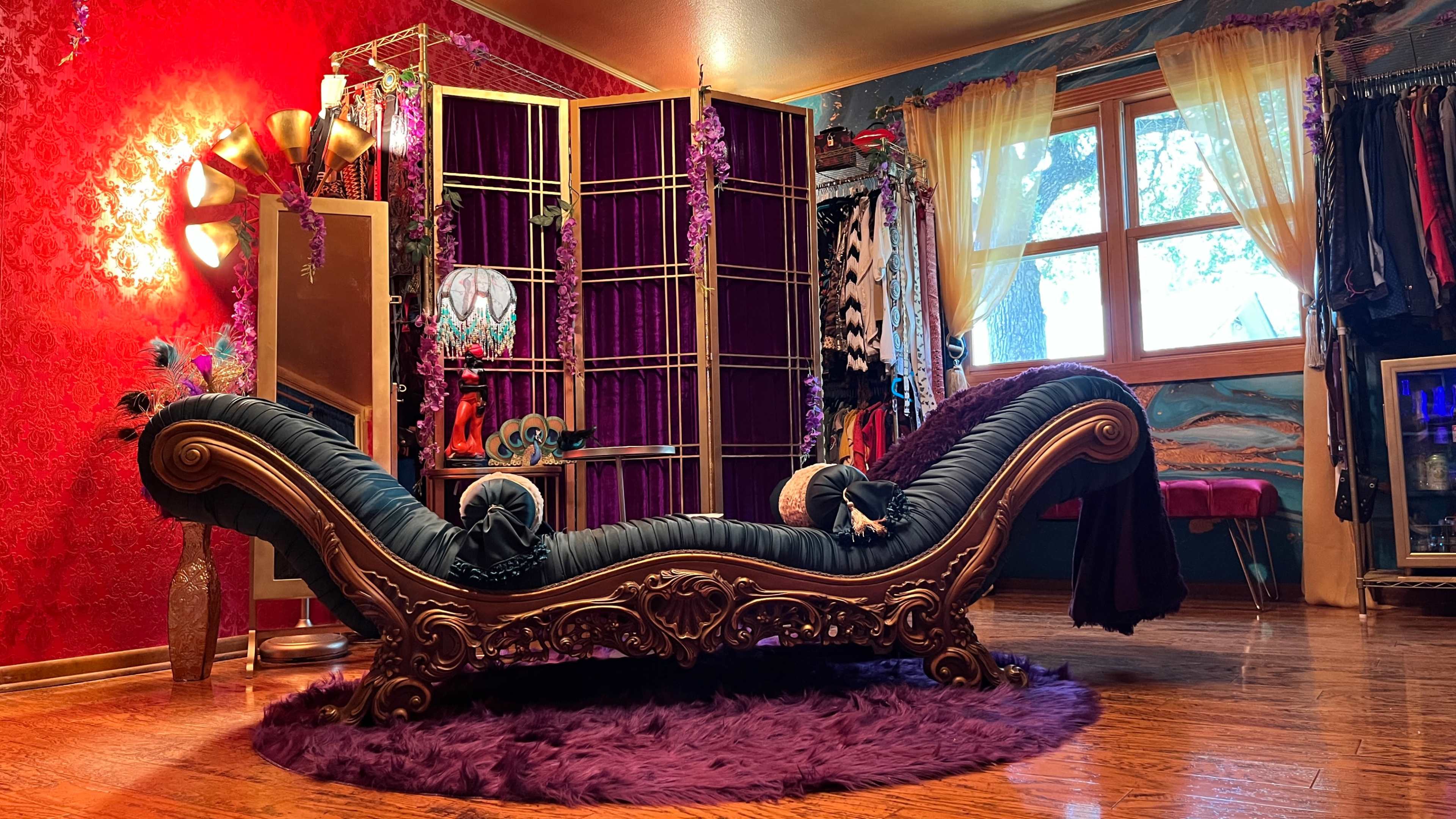 A chaise lounge with ornate detailing is centered in a room adorned with red walls, purple accents, and decorative partitions.