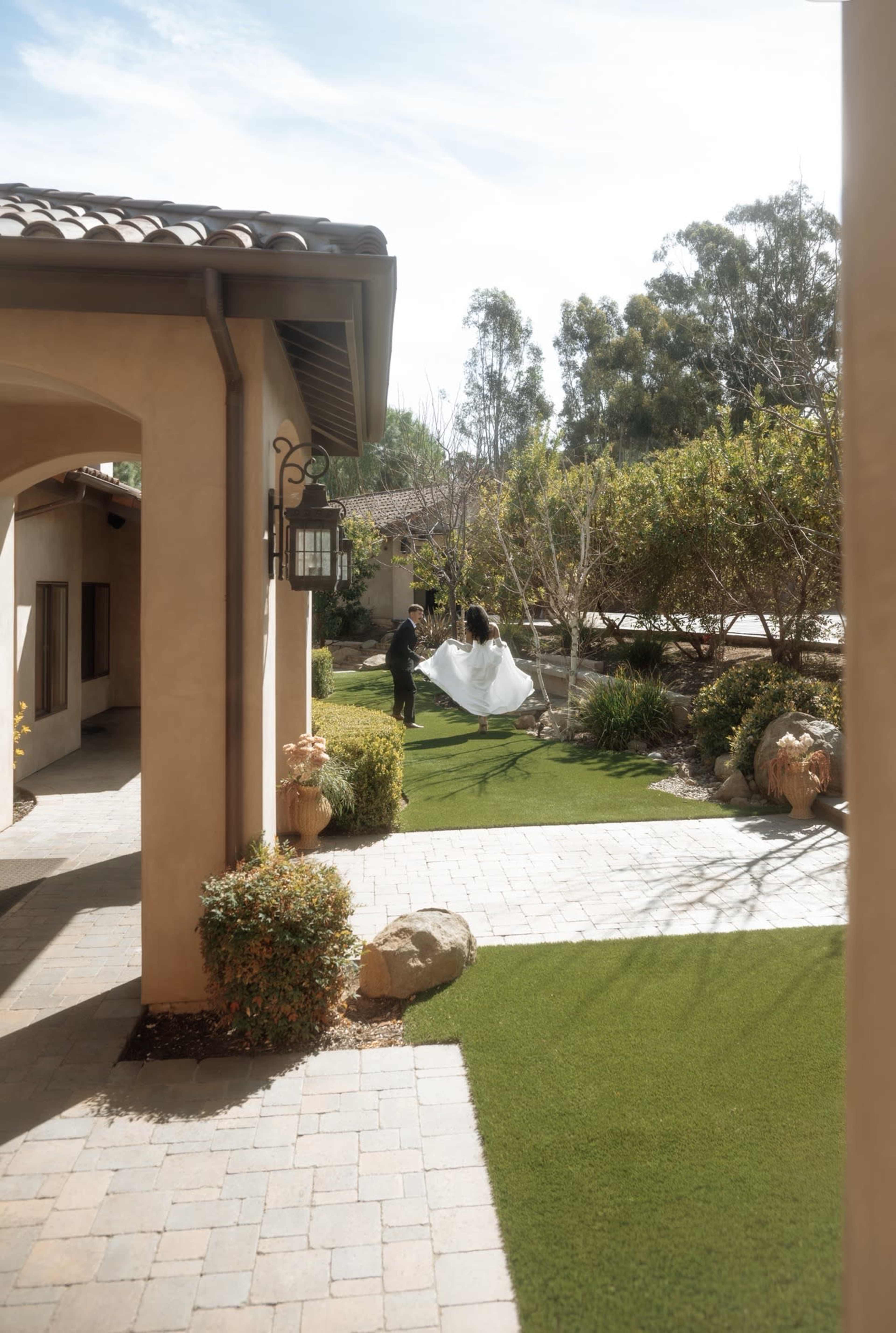 A couple shares a moment in a landscaped garden while walking along a stone pathway next to a house.