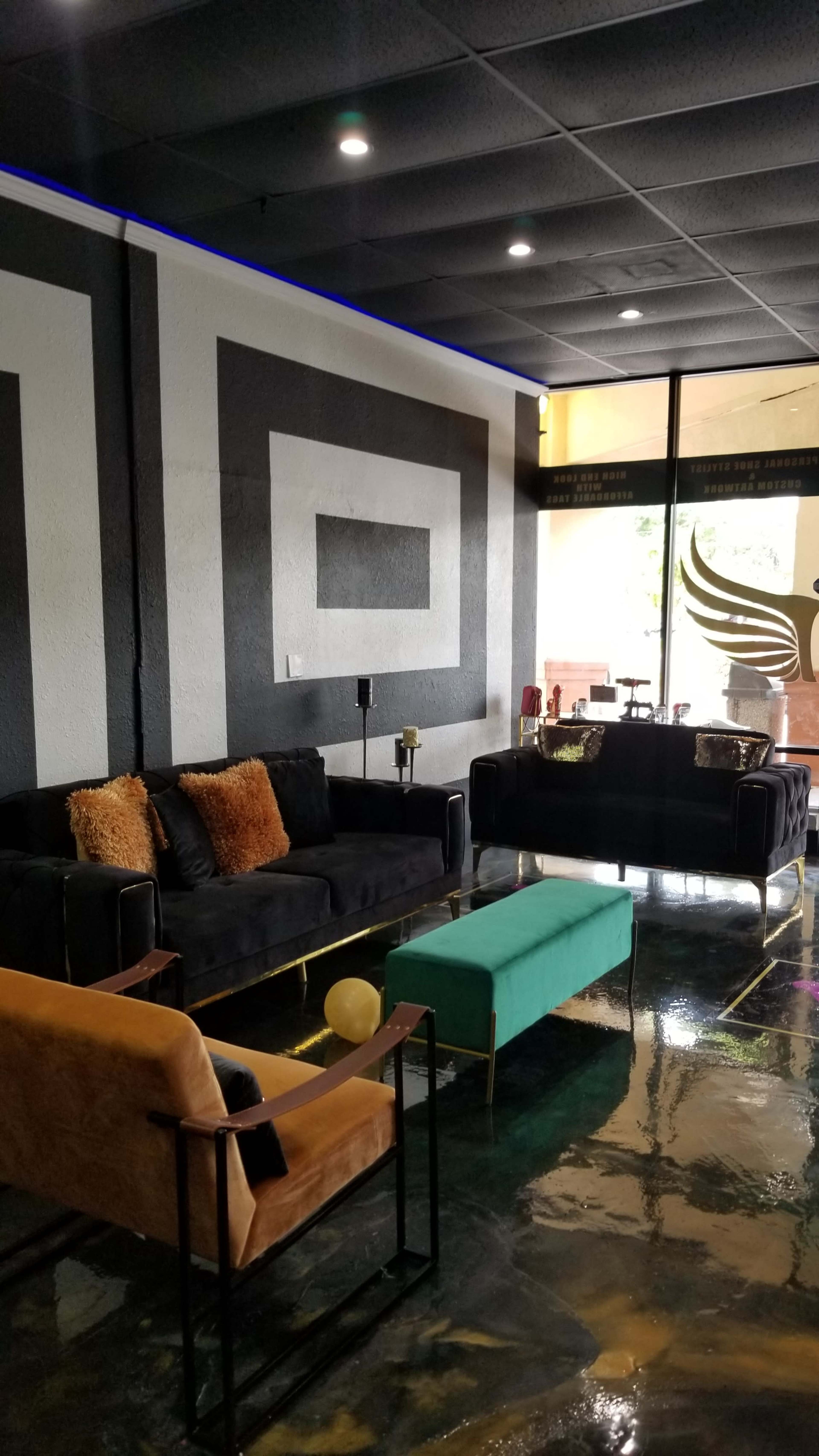 A modern lounge area with black couches, a green coffee table, and a geometric black-and-white wall design.