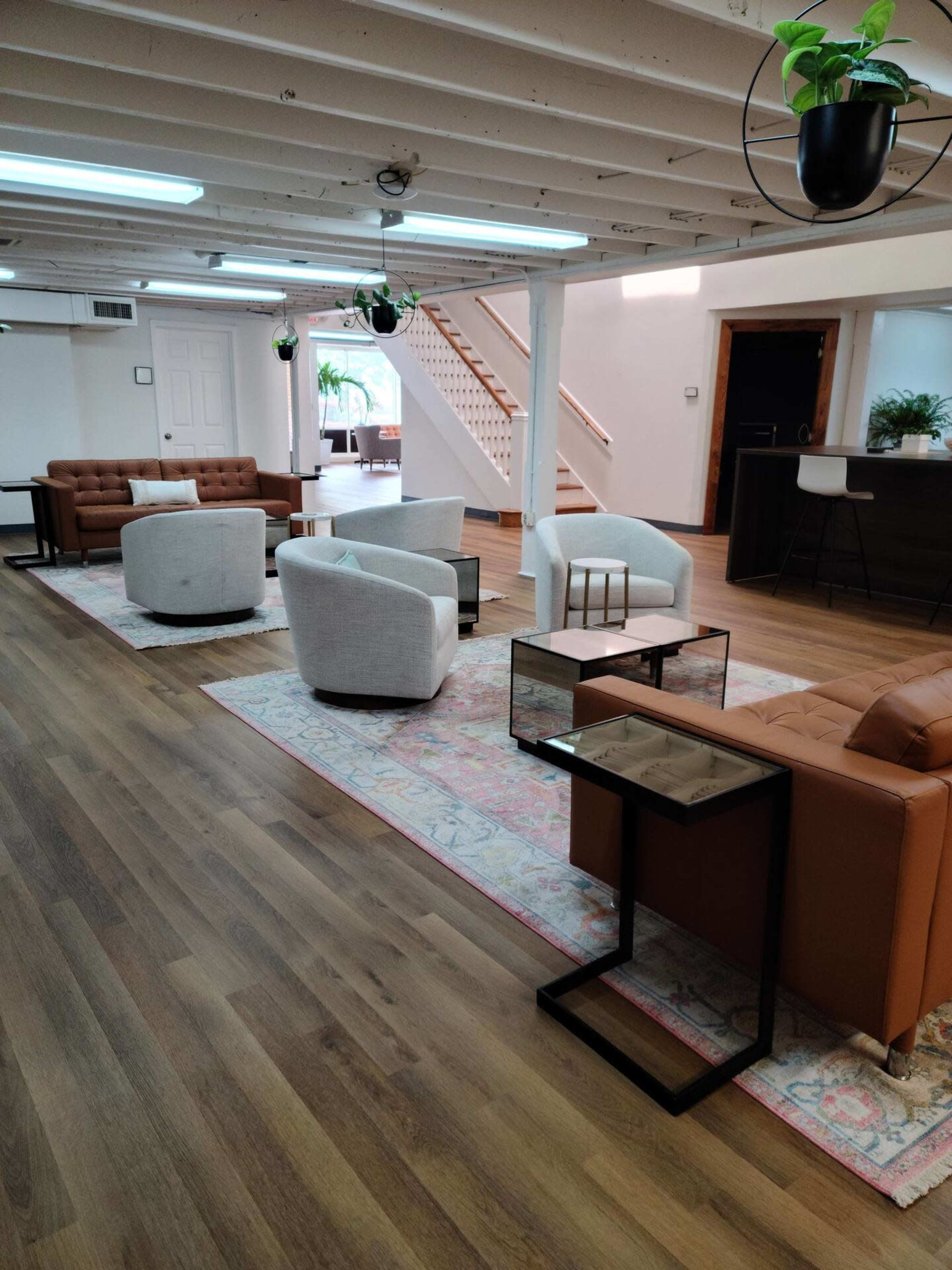 A spacious lounge area with several modern seating arrangements, including sofas and armchairs, set on a wooden floor, with decorative rugs and plants.