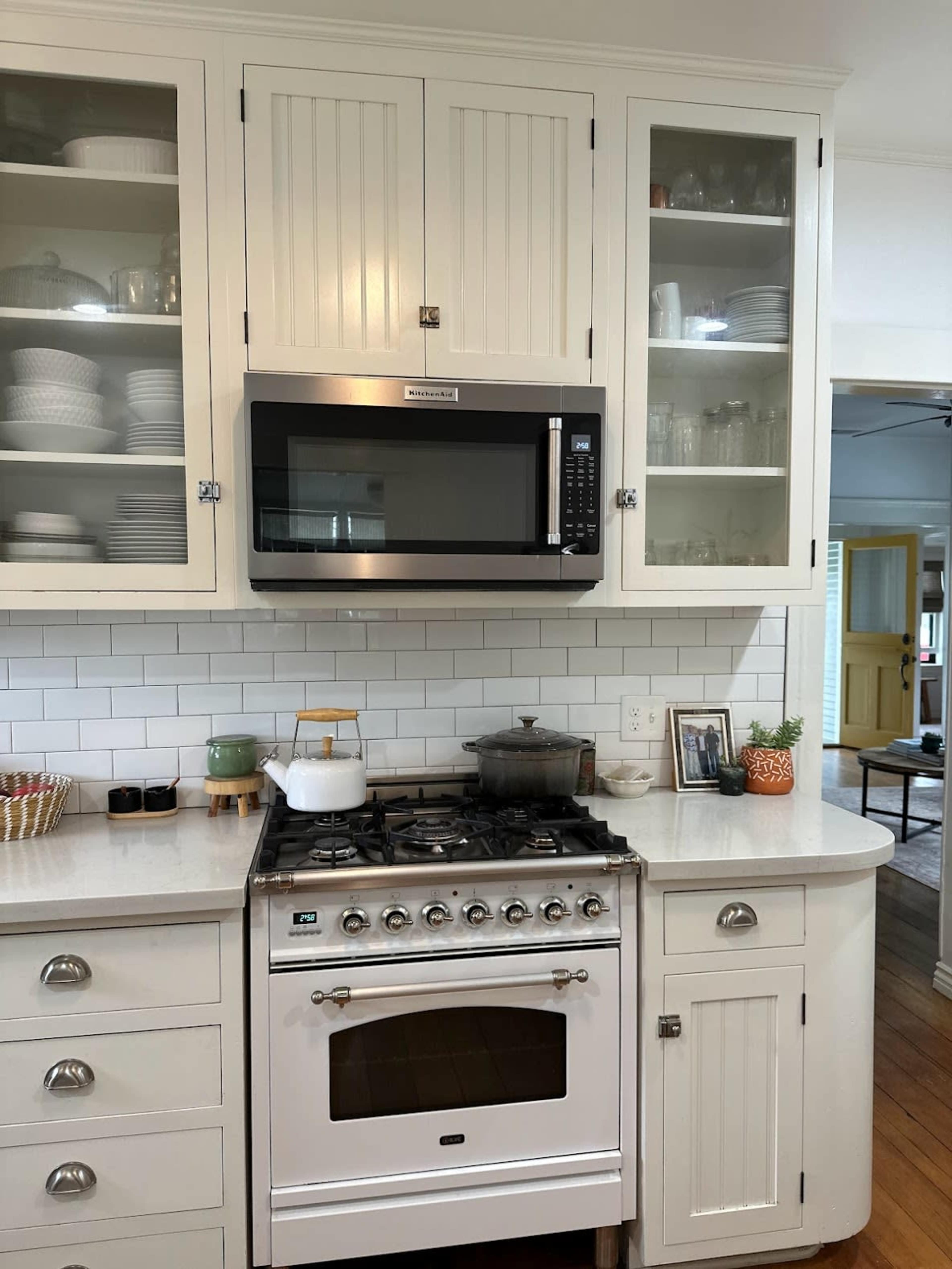 A kitchen featuring a white gas stove, a microwave mounted above it, and cabinets with glass doors displaying dishware.