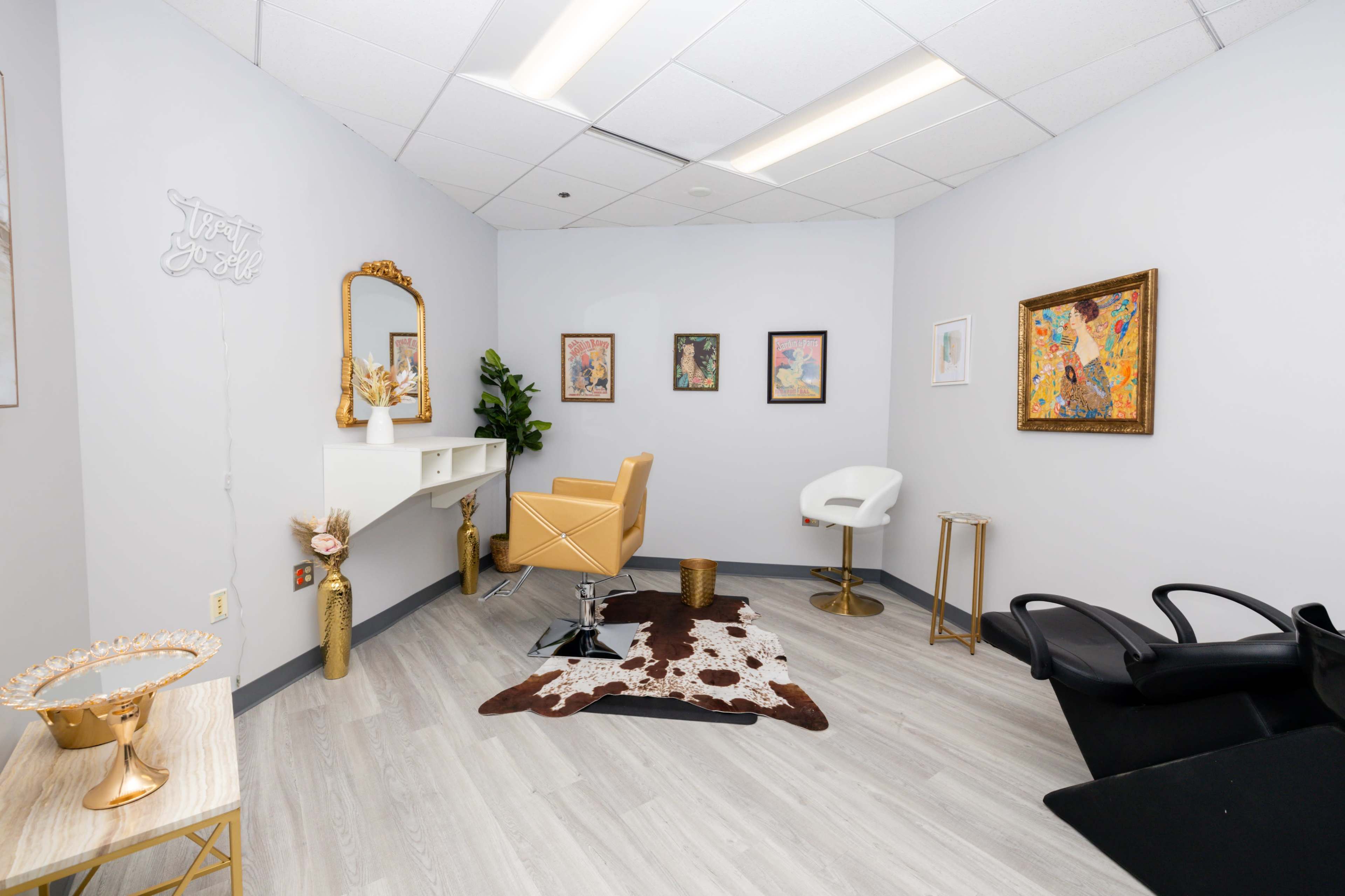 The image shows a modern beauty salon interior with a styling chair, a mirror, a small table, and framed artwork on the walls.