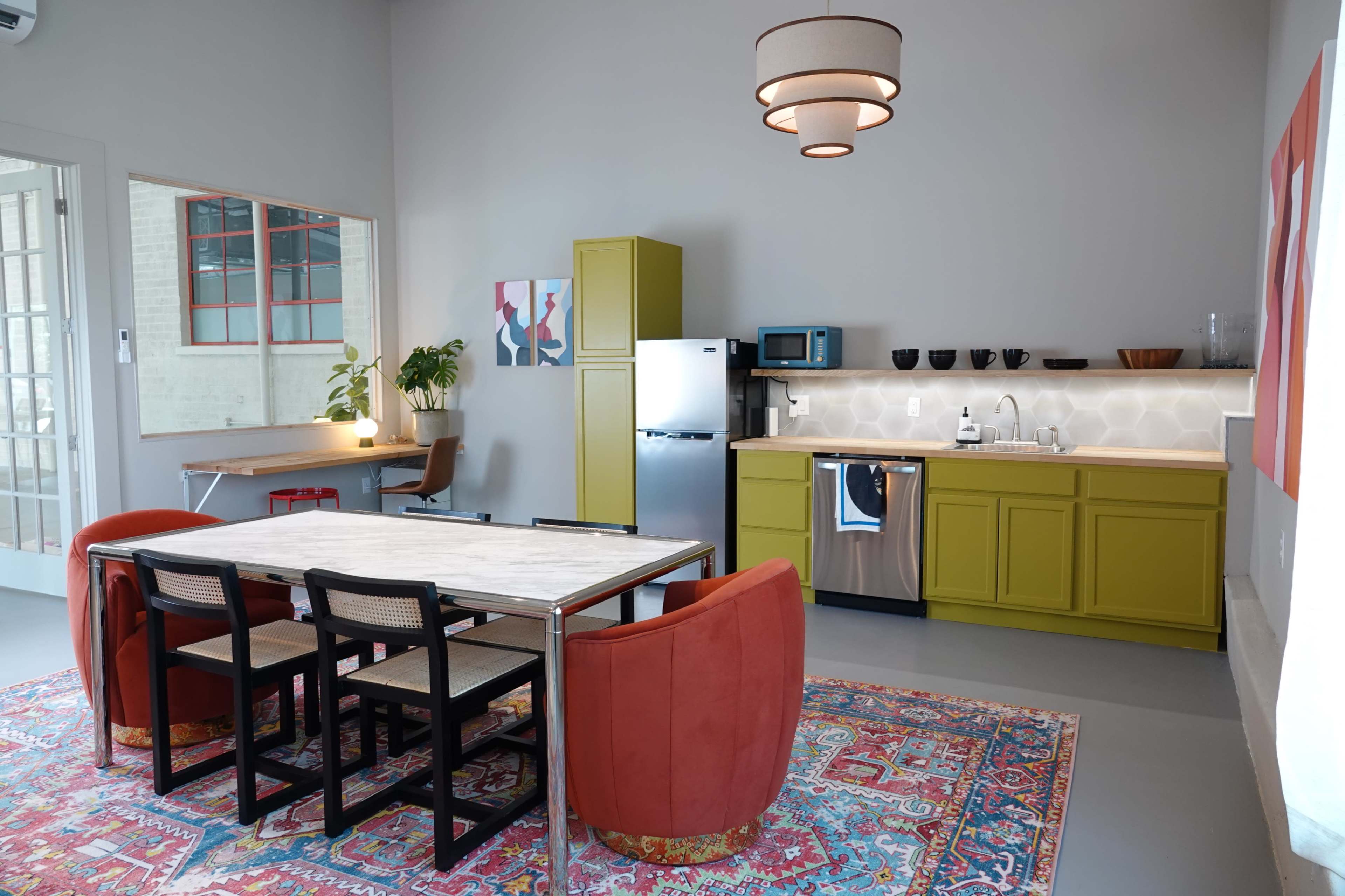 A modern kitchen and dining area featuring a large table with four chairs, a green kitchen cabinet, stainless steel appliances, and a colorful rug on the floor.