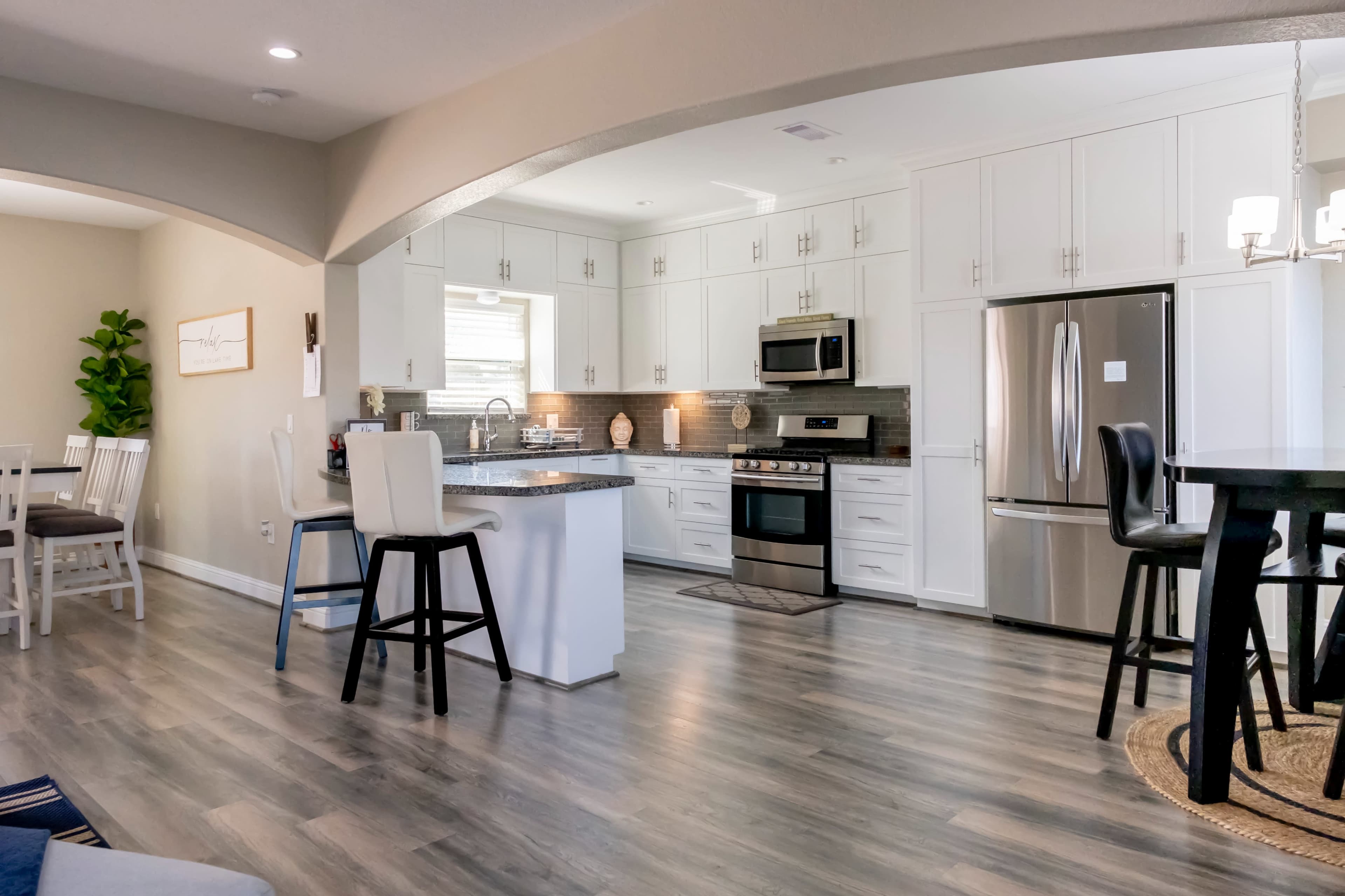 A modern kitchen with white cabinetry, stainless steel appliances, and a large island with bar stools, all set in an open-concept design.