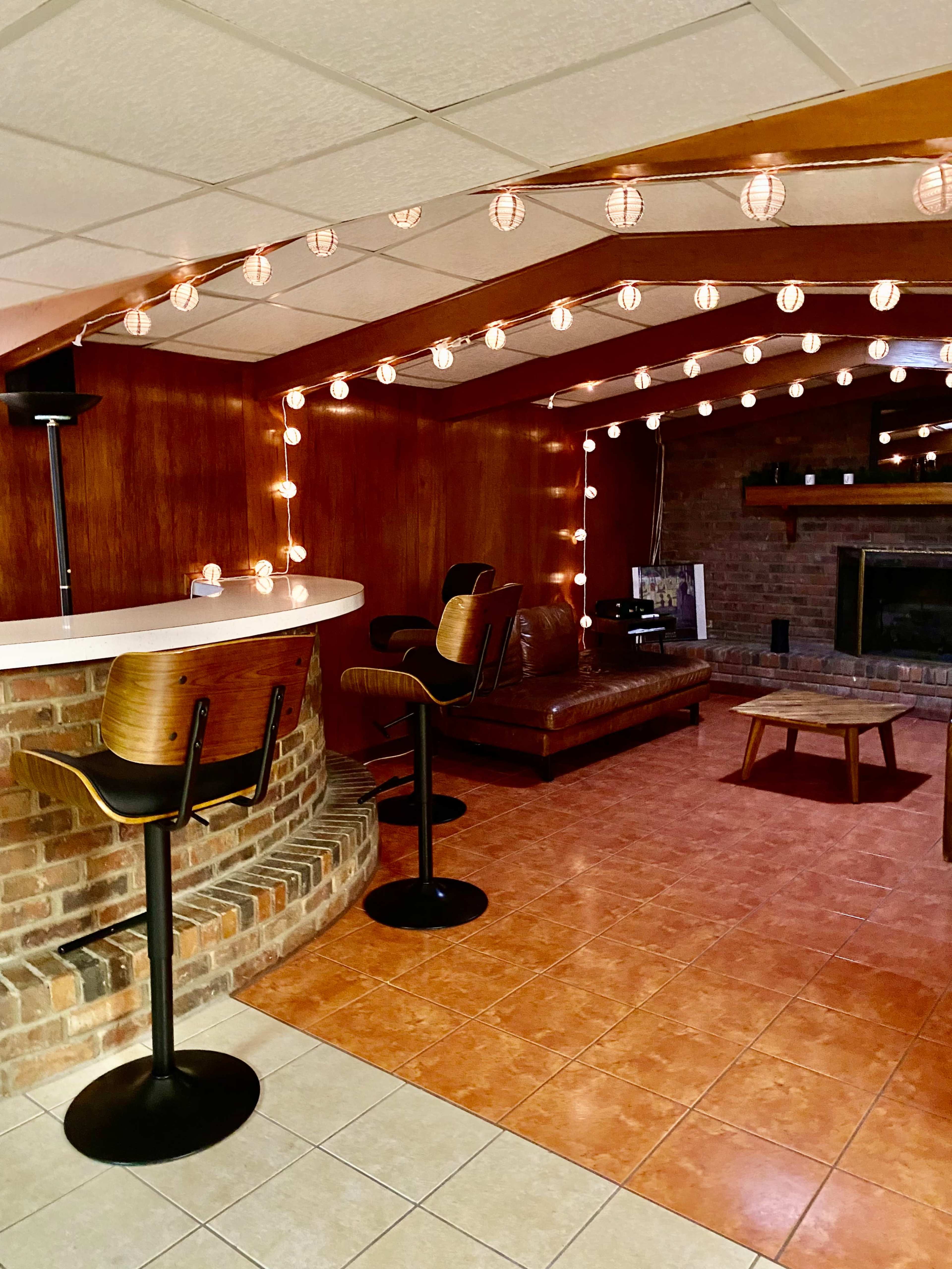 A finished basement with a bar area, seating, and decorative string lights.