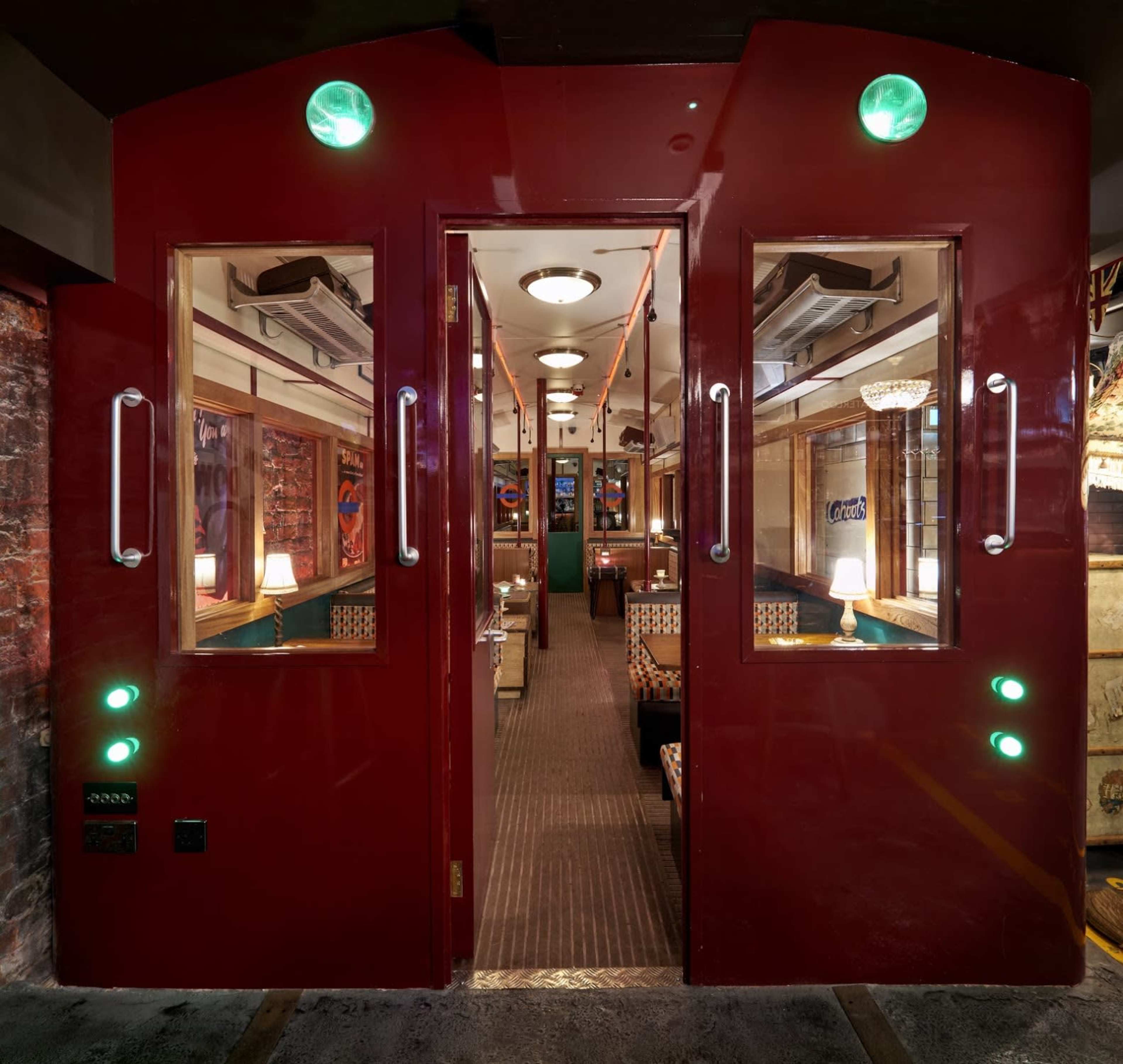 The entrance to a restaurant designed to resemble a train carriage features bright red doors and green lights, with a visible dining area inside.