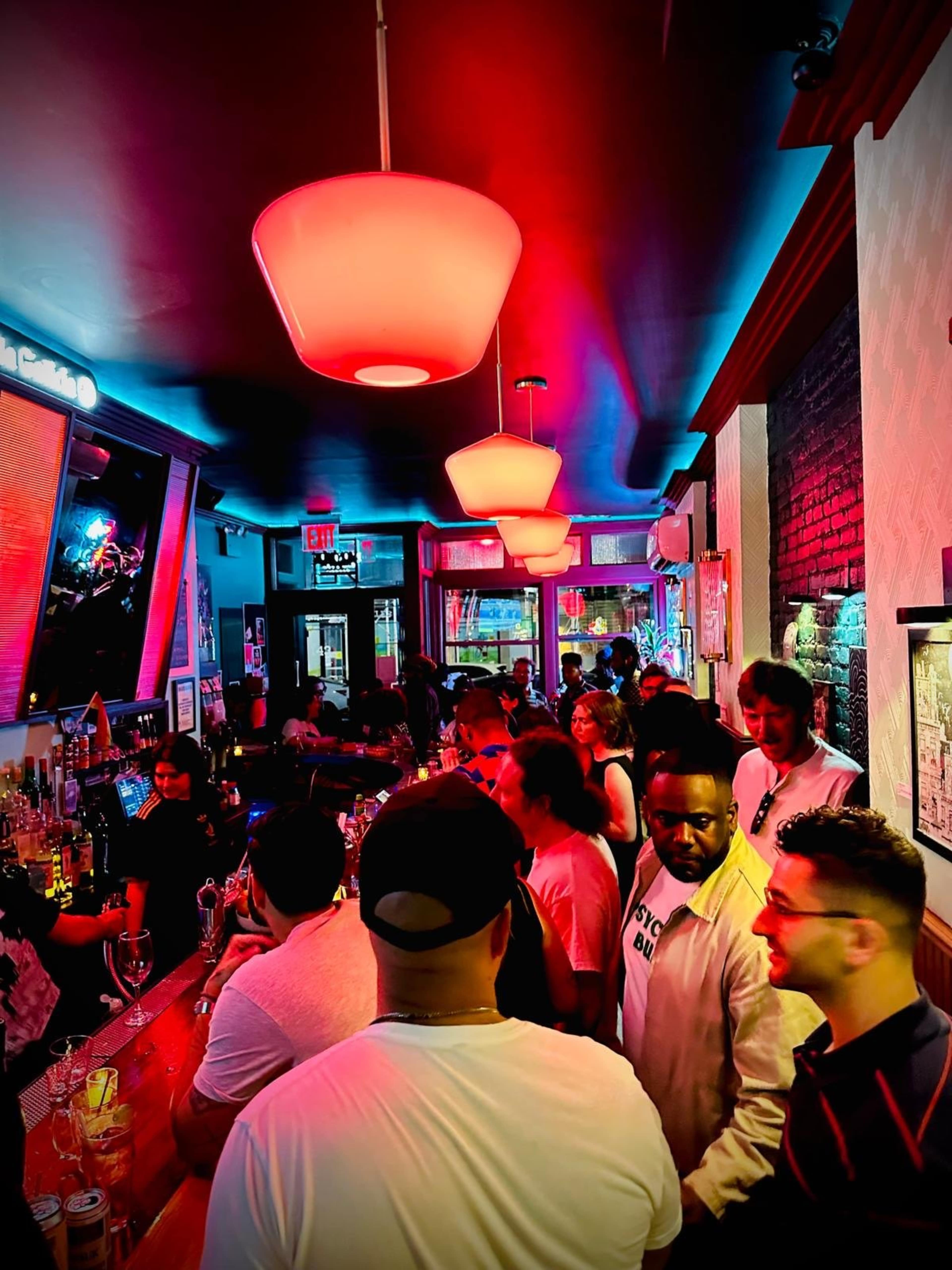 A lively bar scene filled with patrons conversing and enjoying drinks under colorful lighting.