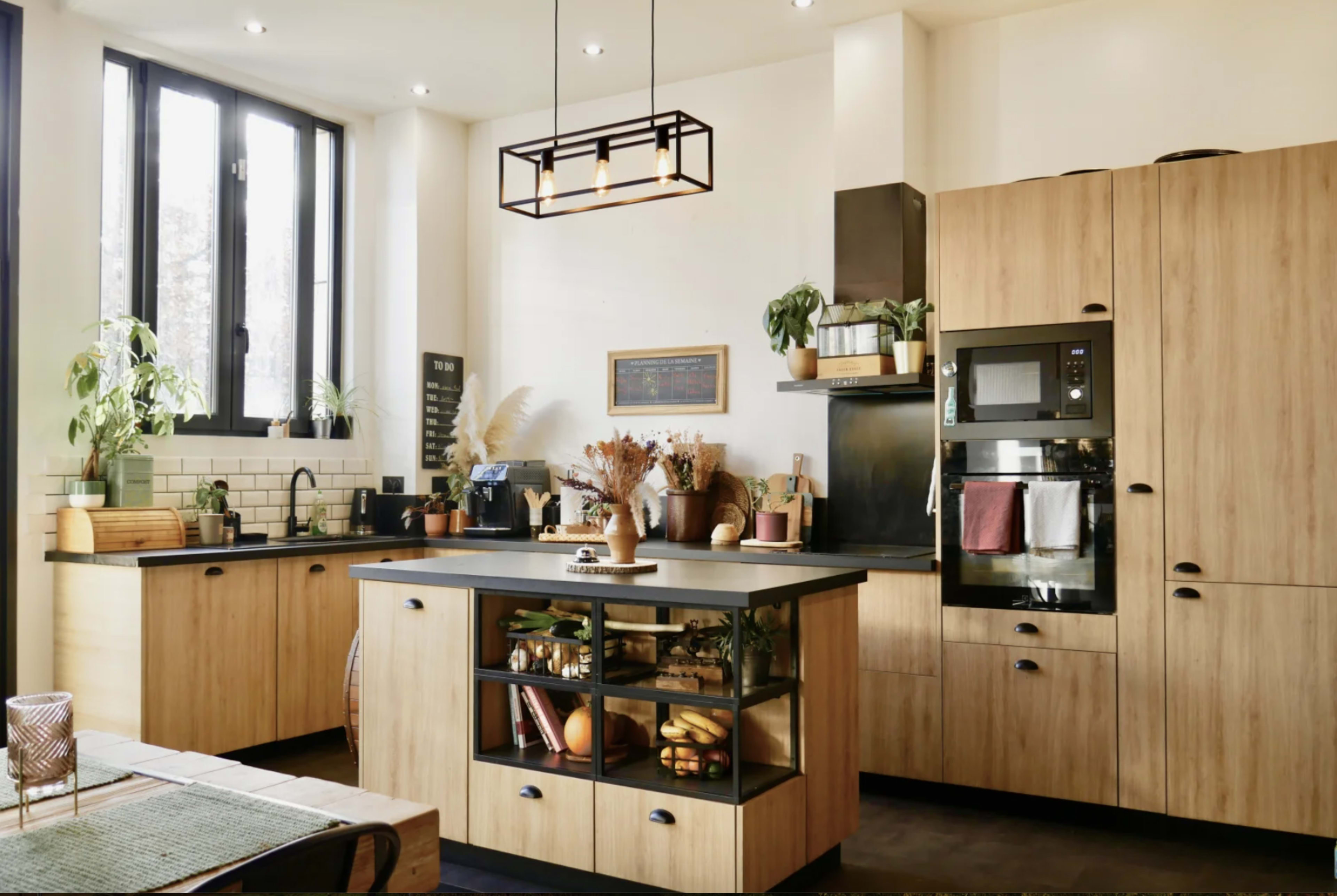 A modern kitchen features wooden cabinetry, an island with a glass front displaying fruits, and various kitchen appliances against a light backdrop.