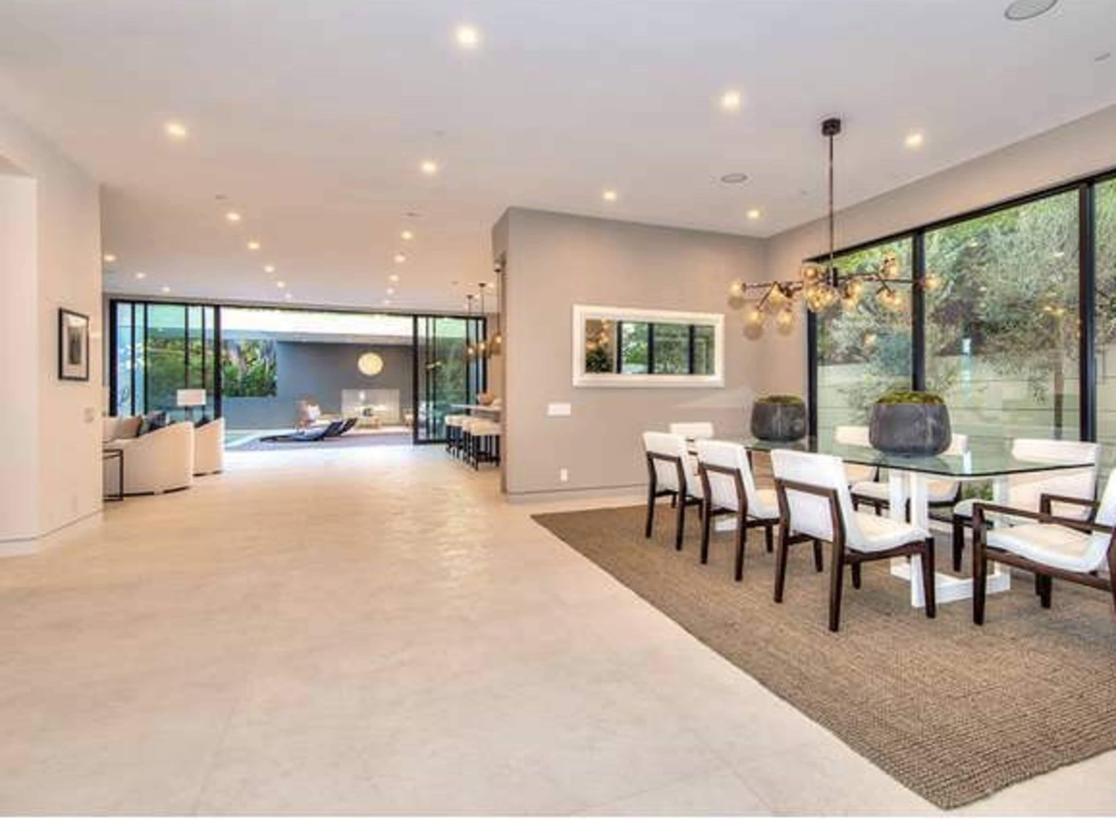 The image shows a modern open-concept living and dining area with large windows and a view of an outdoor space.