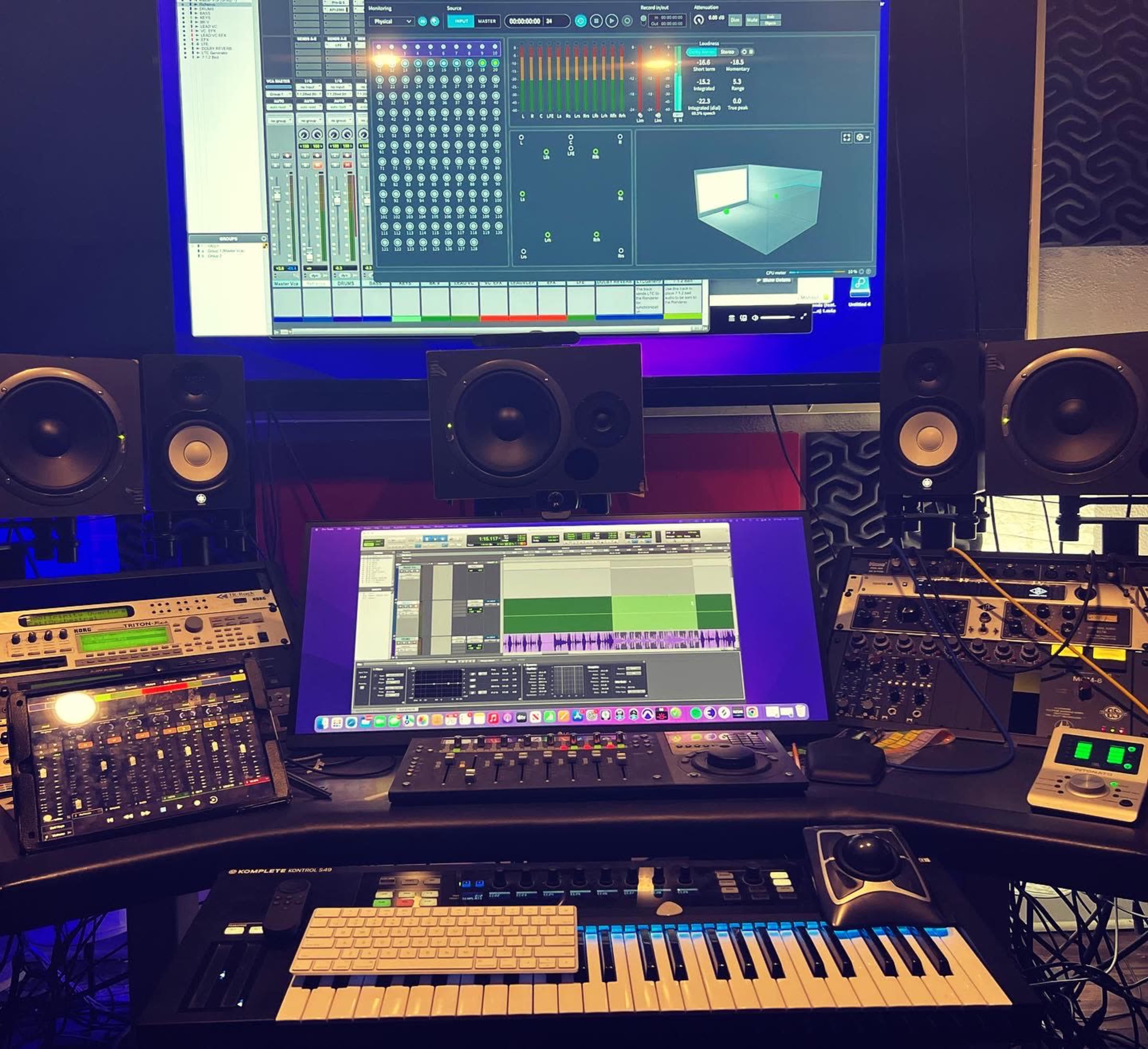 A digital audio workstation setup featuring multiple monitors, audio equipment, and a MIDI keyboard in a music production studio.