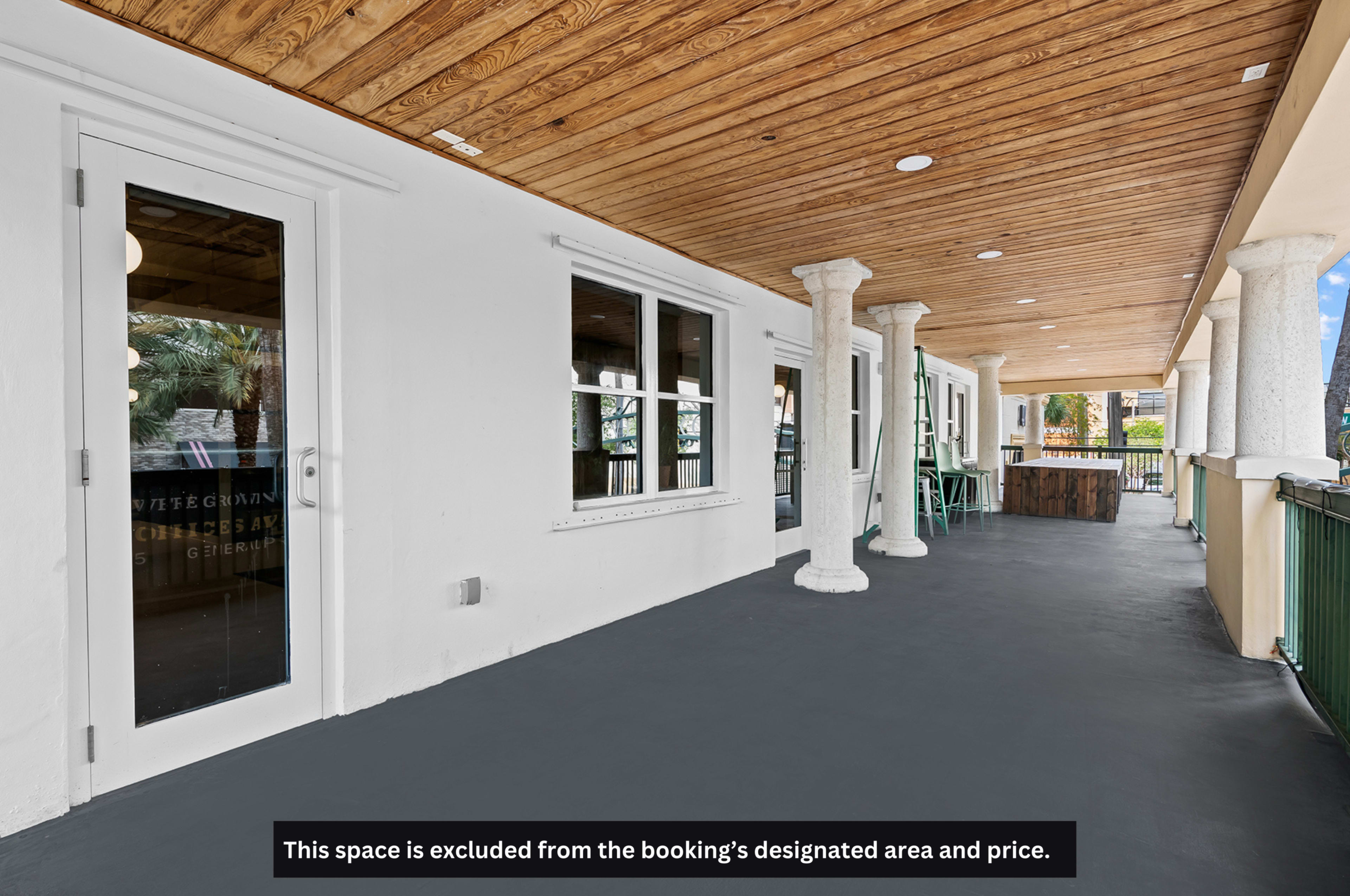 The image shows a covered porch area with a wooden ceiling, columns, and several tables and chairs along the railing.