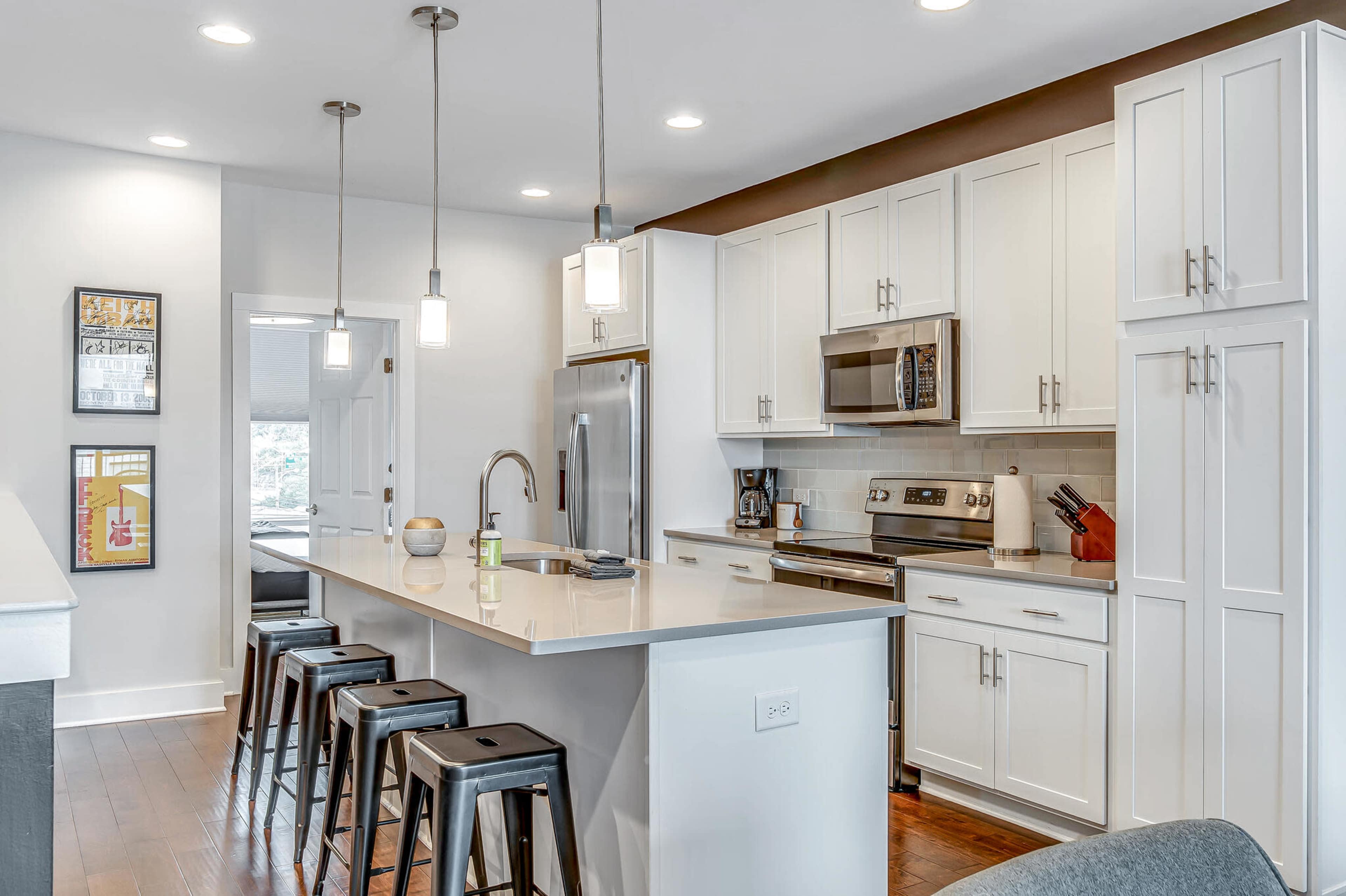 A modern kitchen features white cabinetry, stainless steel appliances, and a central island with bar stools.