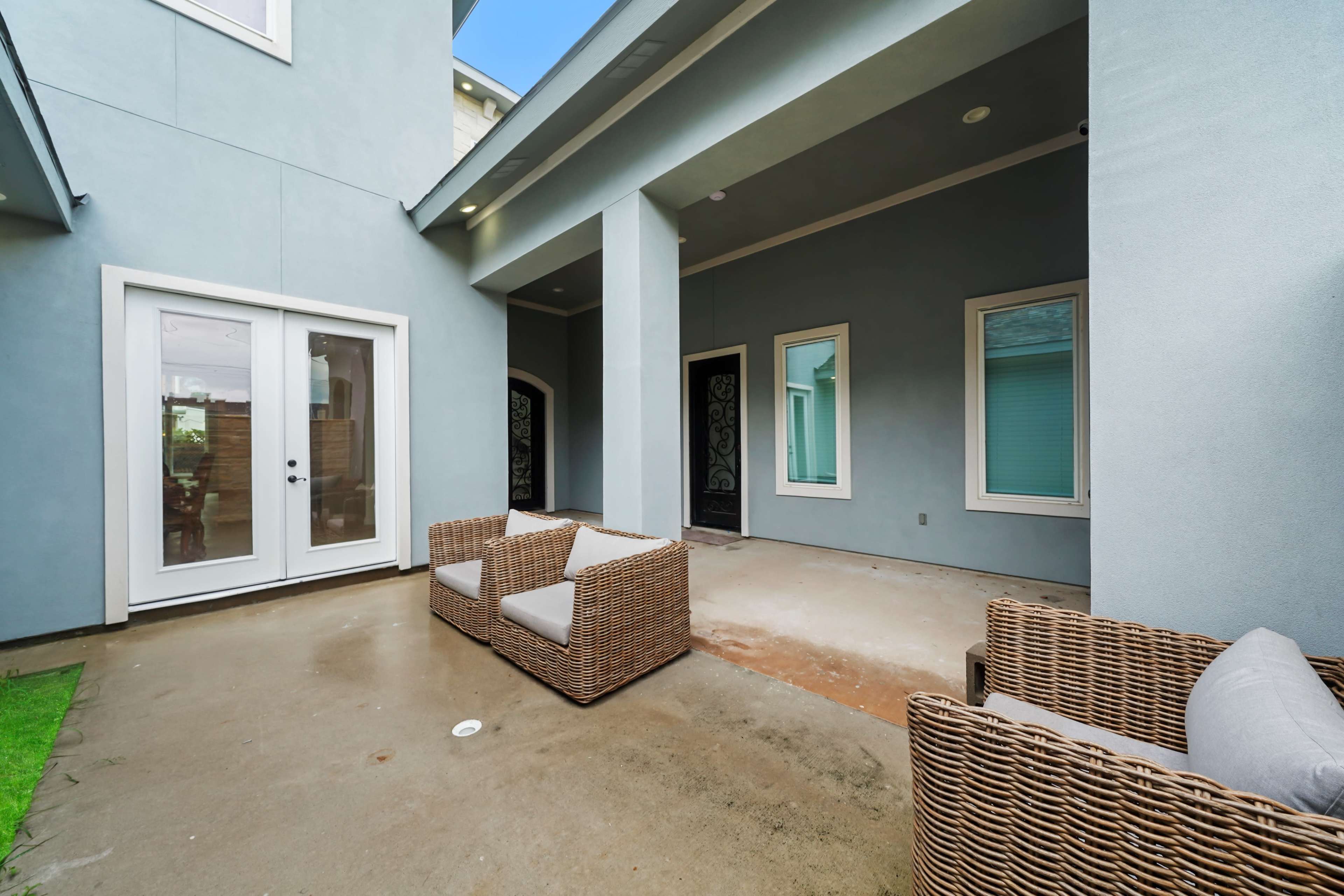 The image shows a small outdoor patio with two wicker chairs and a sliding glass door leading into a house.