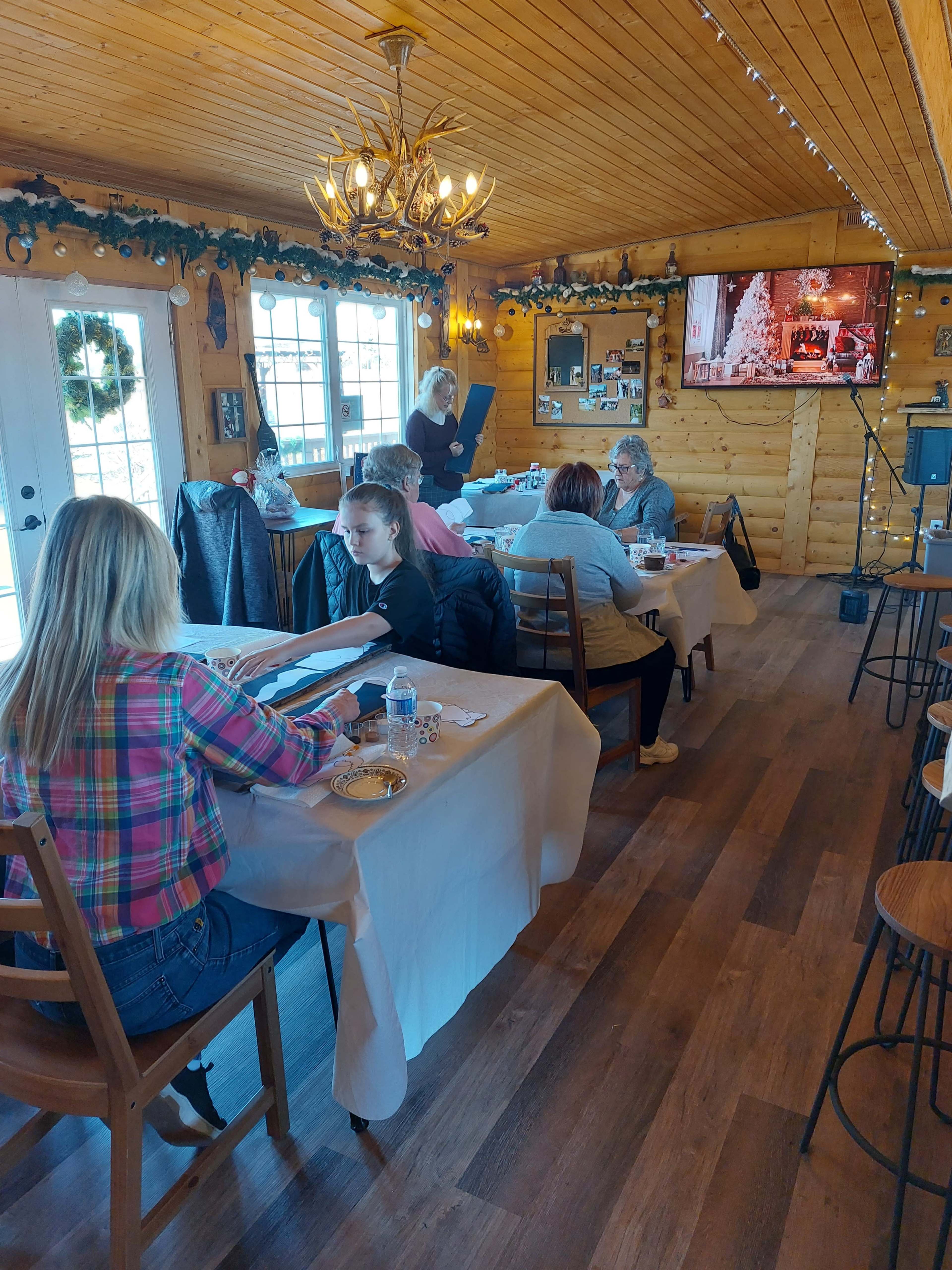 A cozy dining room features several tables where guests are seated, and a television displaying holiday decorations is mounted on the wall.