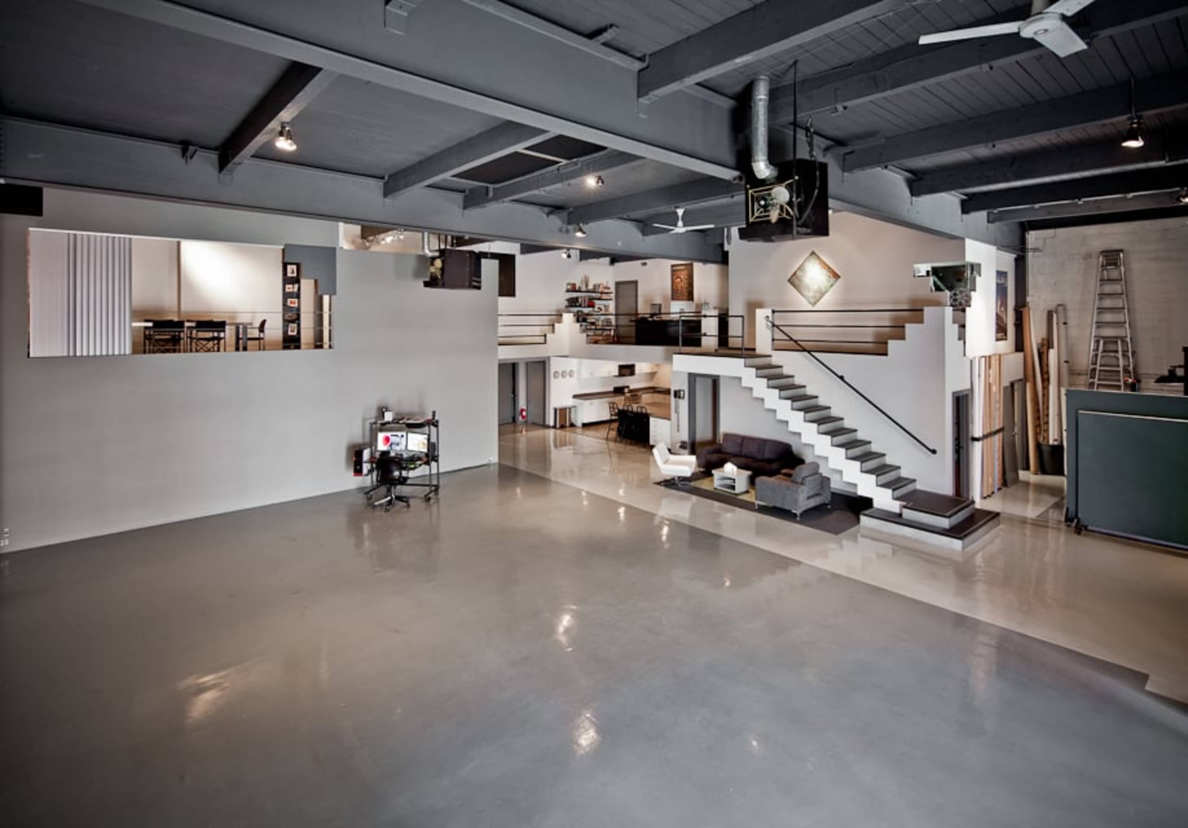 A spacious industrial-style loft features an open floor plan with a modern kitchen, dining area, and living space on multiple levels.