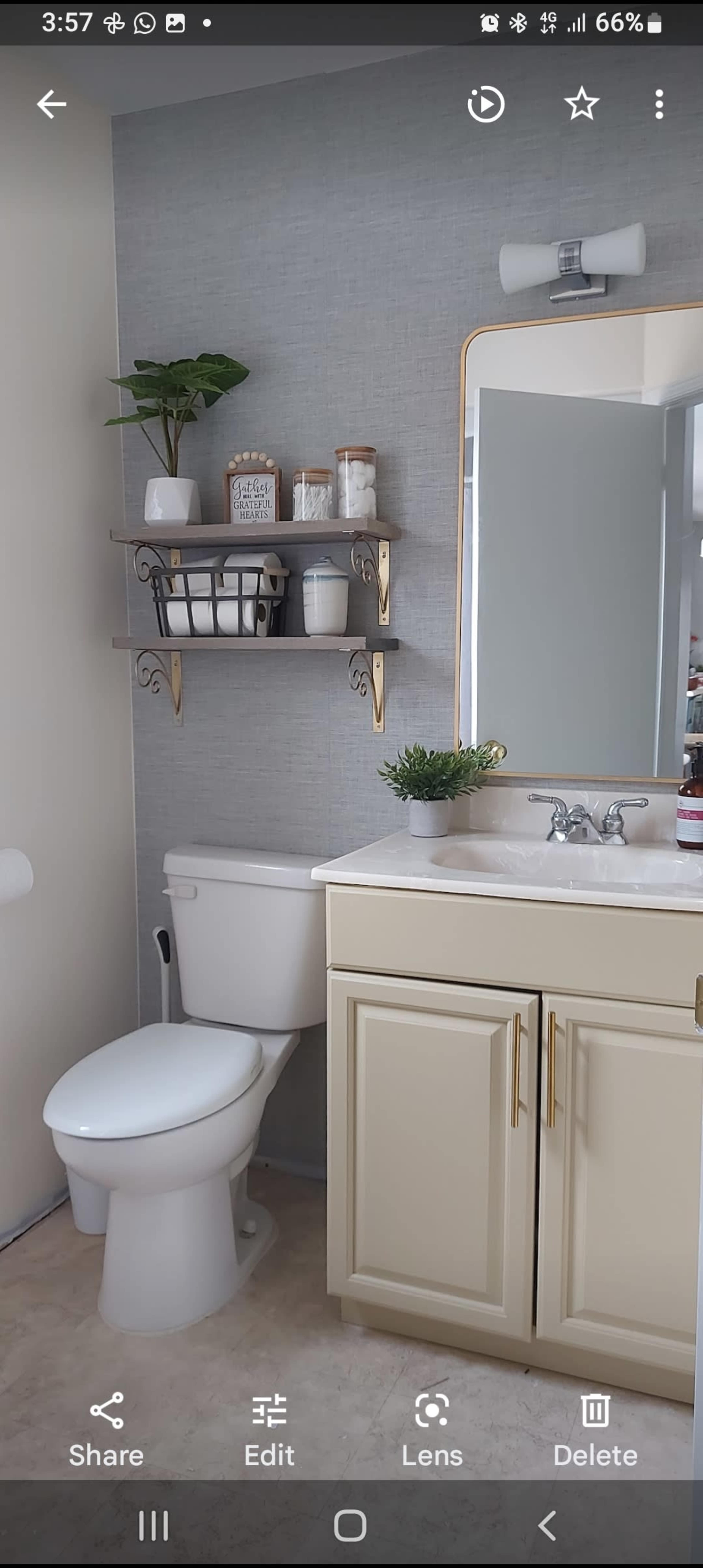 A bathroom featuring a toilet, a sink with cabinets, a mirror, and a wall-mounted shelf with decorative items.