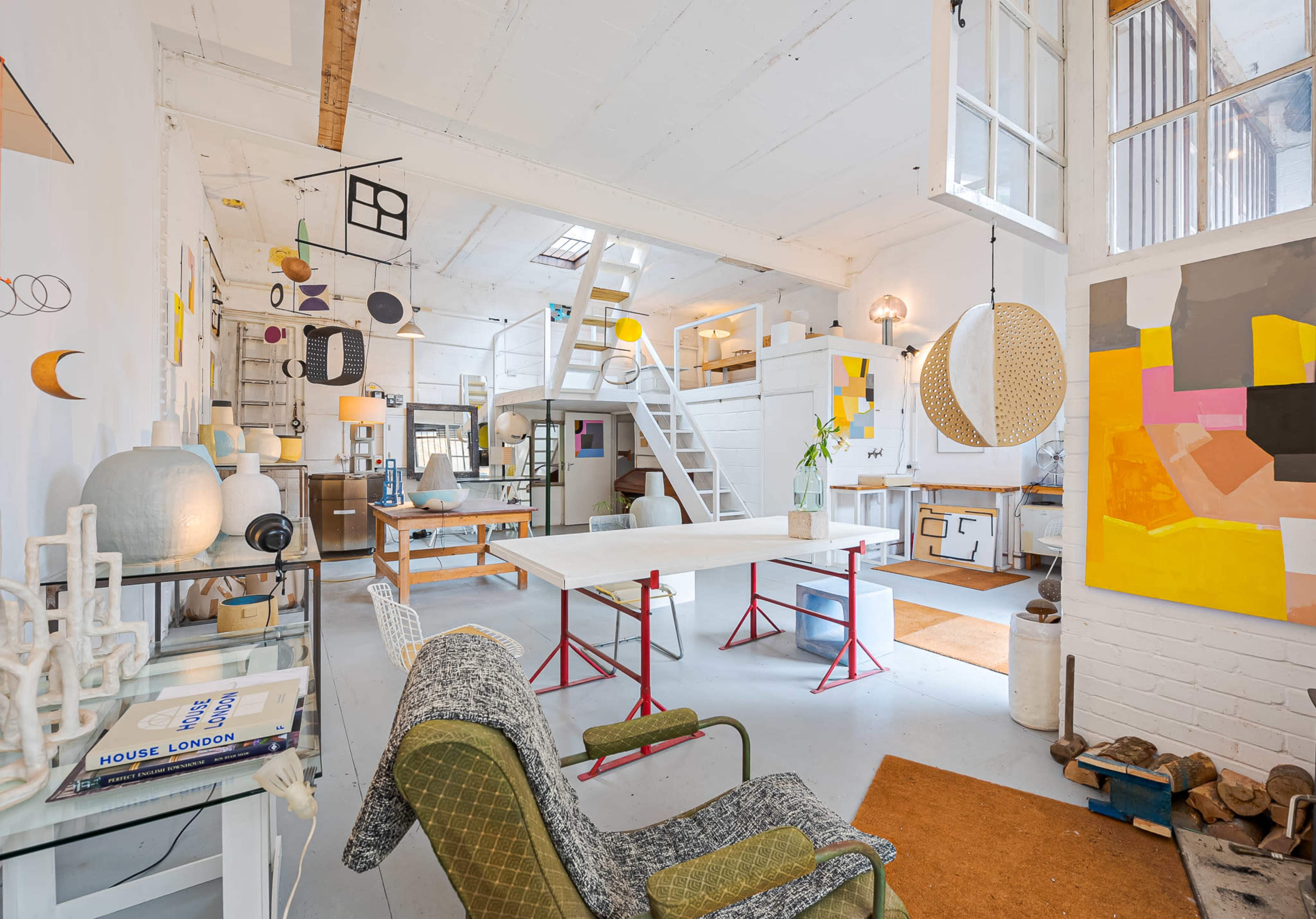 The image shows a spacious, well-lit studio with various art pieces, furniture, and a large table at its center.