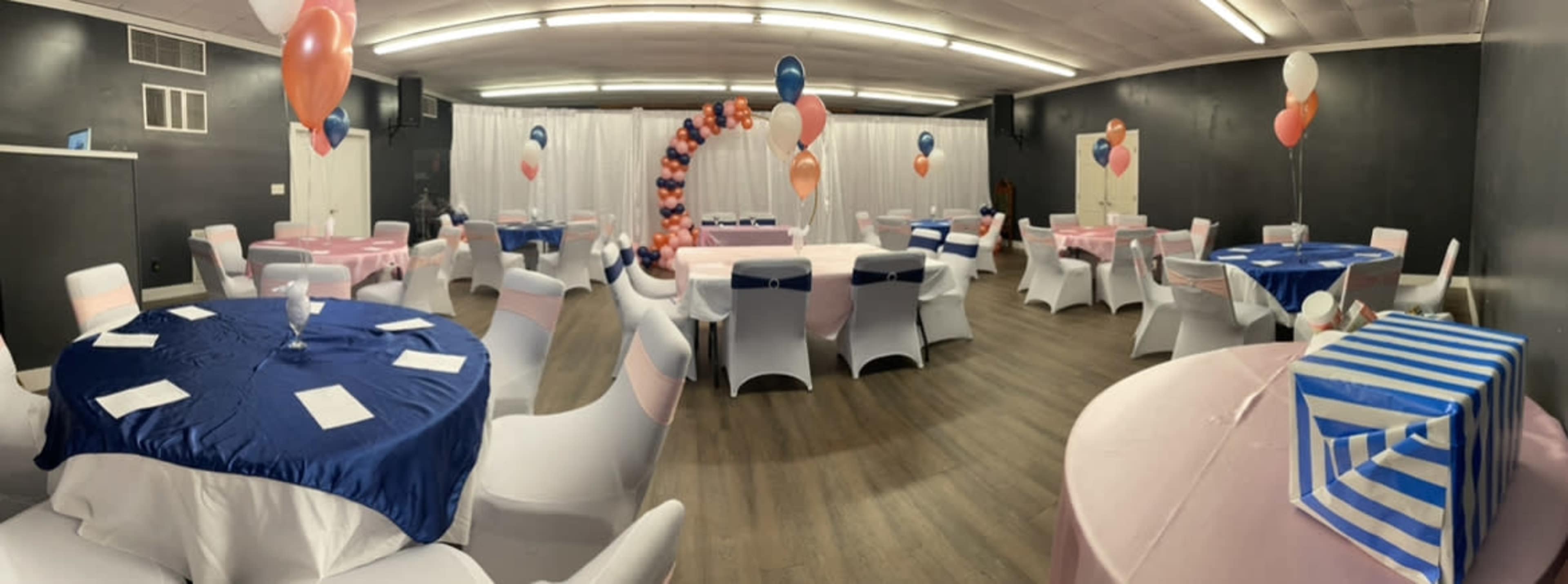 A decorated event space with tables covered in pastel linens, balloons, and an arch made of balloons.