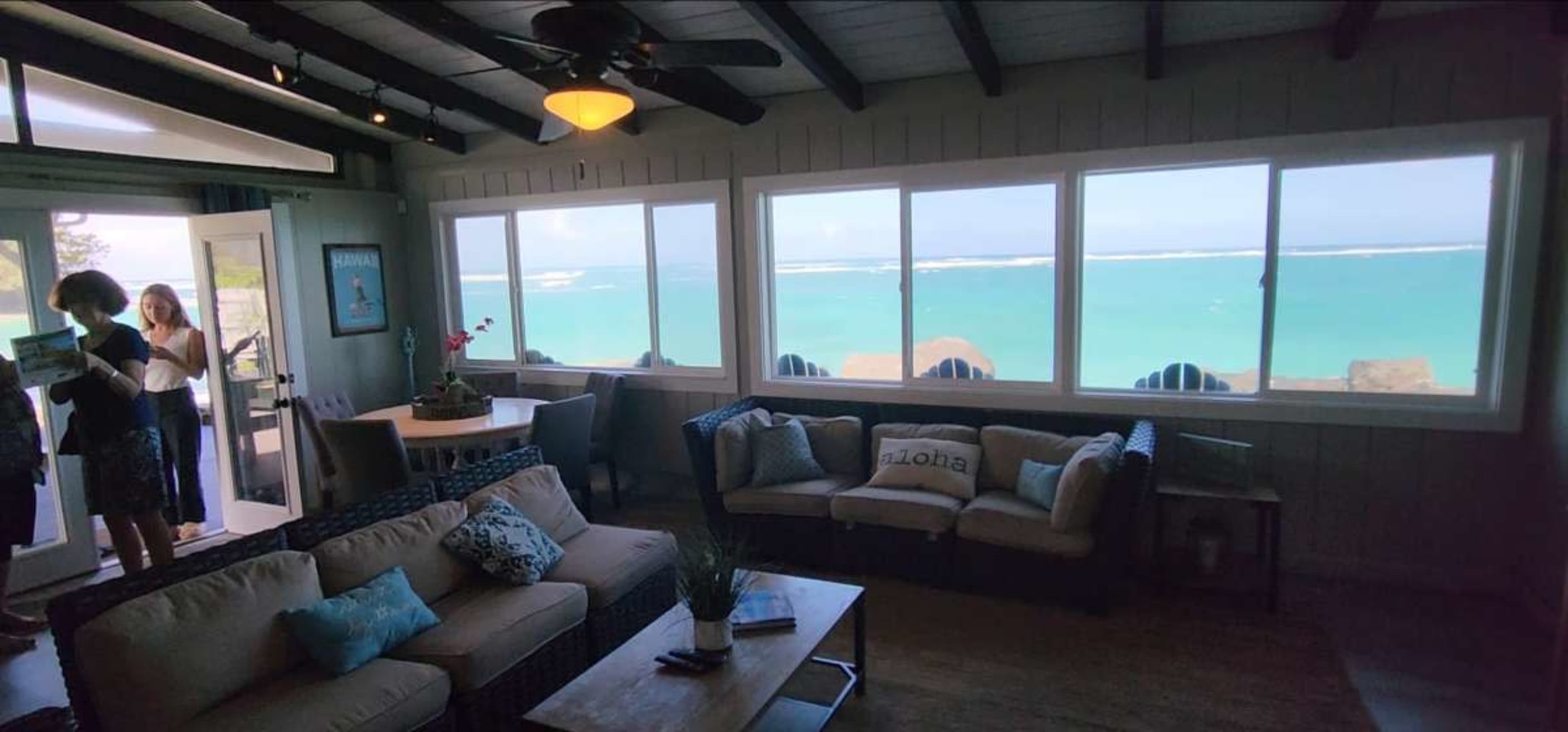 A cozy living room features a sofa and a coffee table, with large windows showcasing a view of the turquoise ocean beyond.