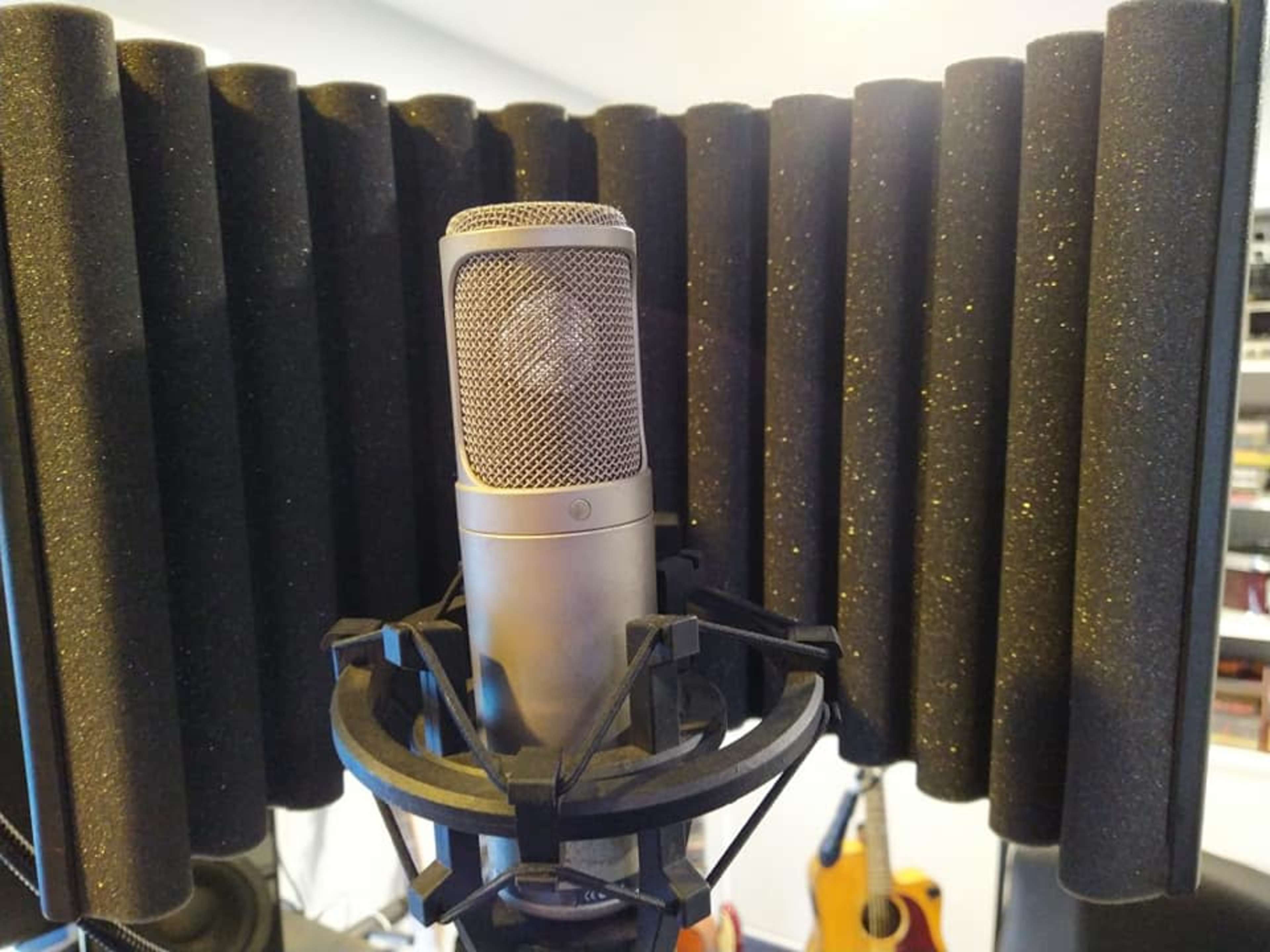 A microphone is positioned in front of a sound isolation shield made of multiple foam panels.