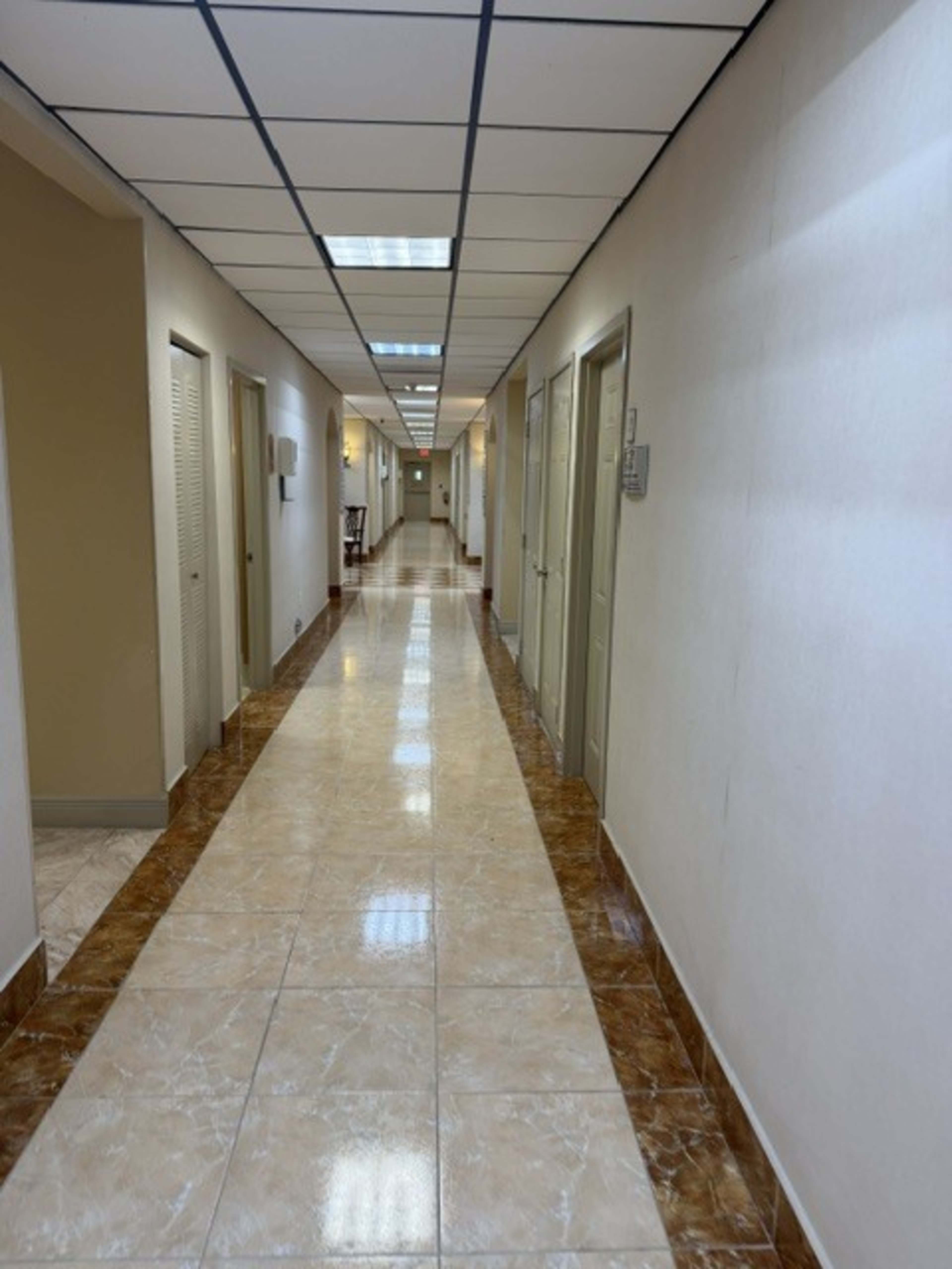 The image shows a long, well-lit corridor with doors on either side and a tiled floor.
