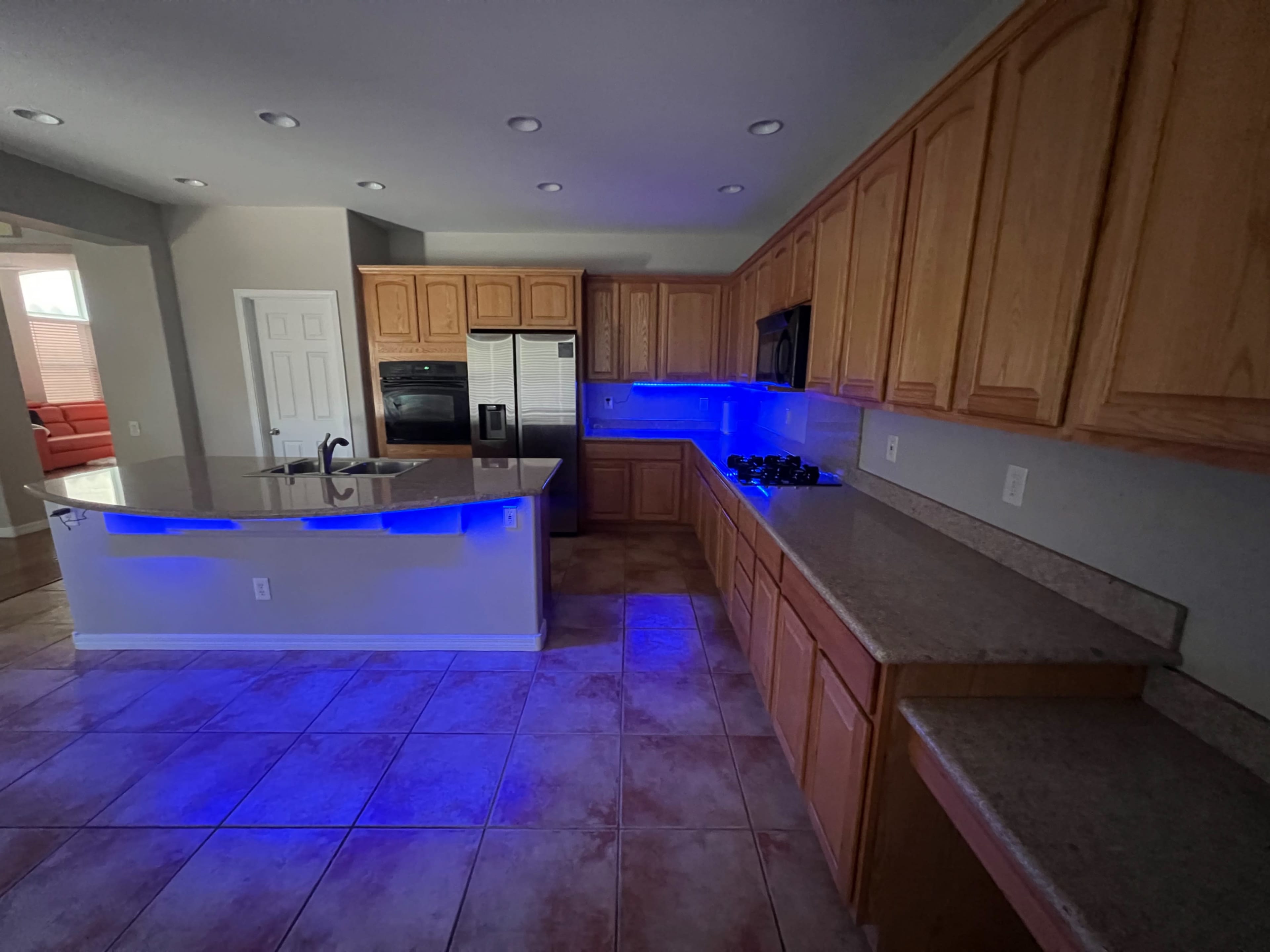 The kitchen features wooden cabinetry, a spacious island, and blue LED lighting along the countertops.