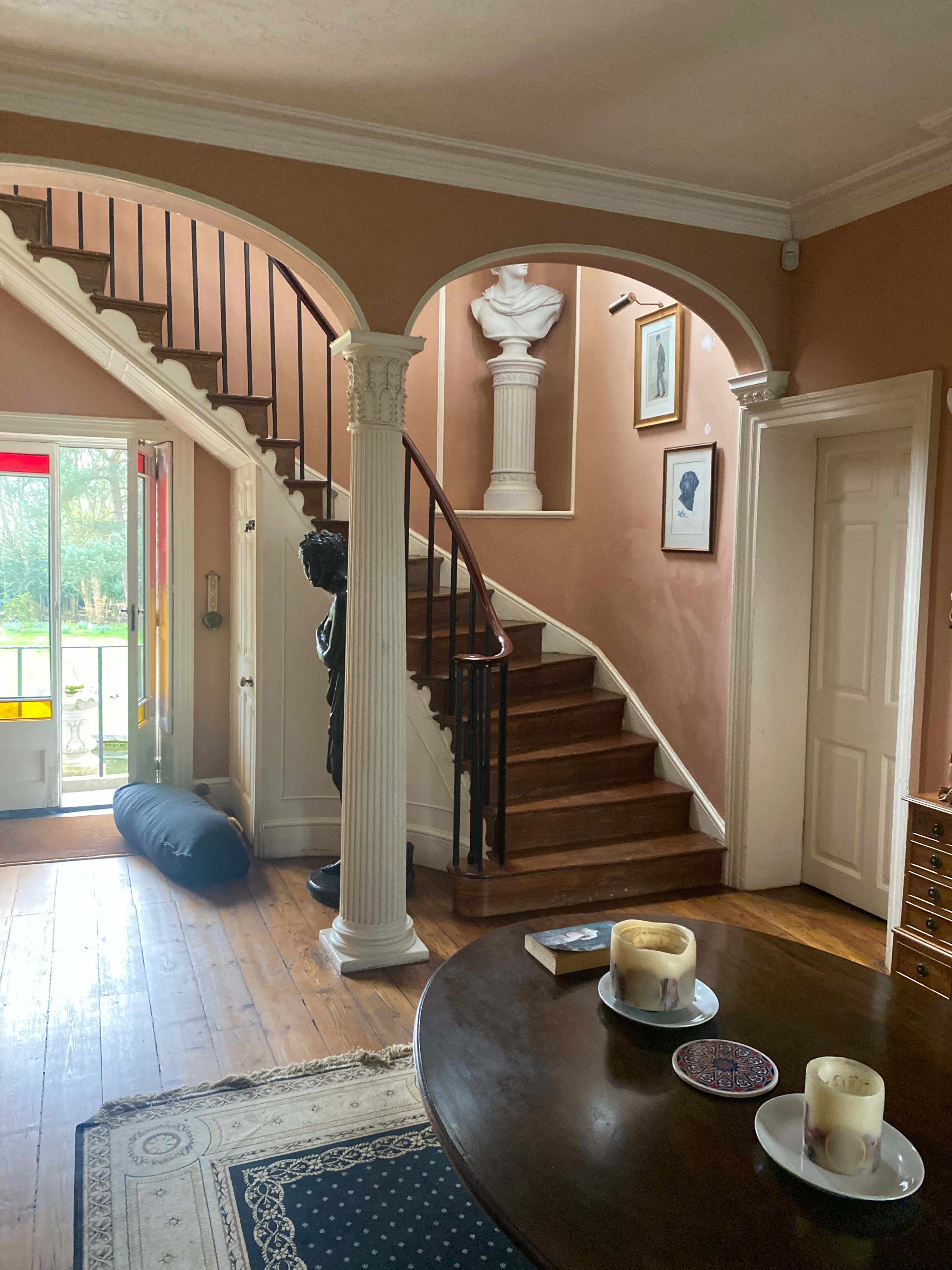 A foyer with a curved staircase, flanked by decorative columns, and a view of a front door illuminated by natural light.