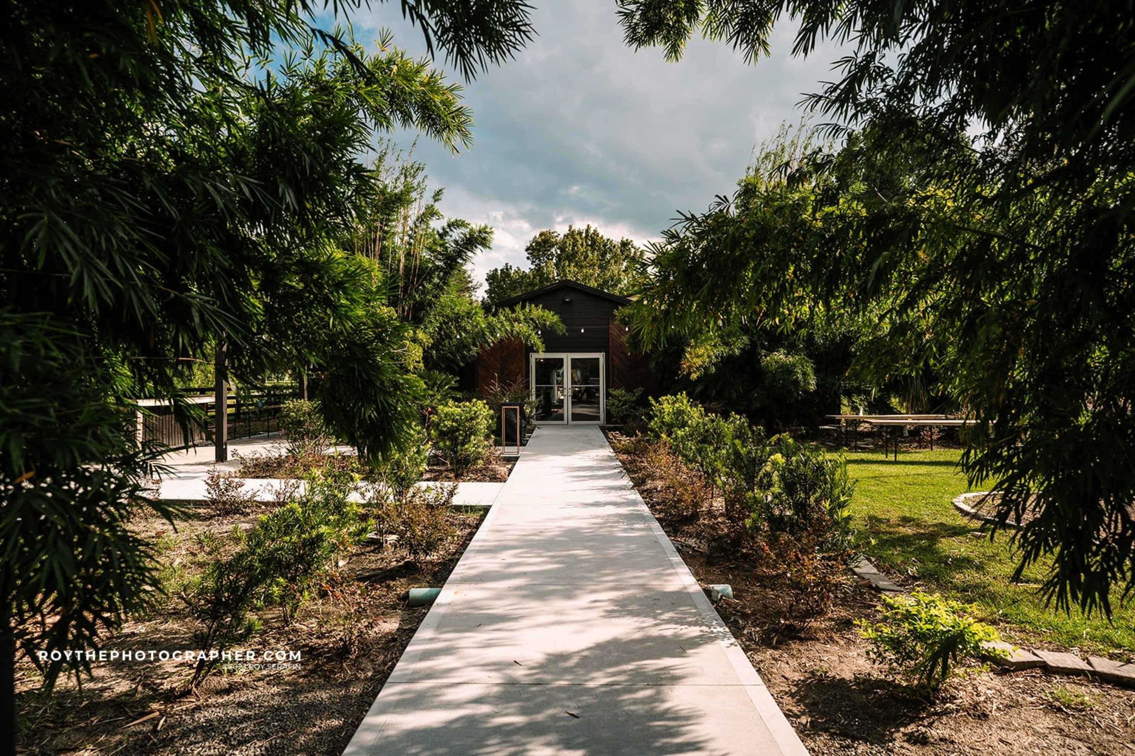 A concrete pathway leads to a modern building surrounded by lush greenery and garden areas.